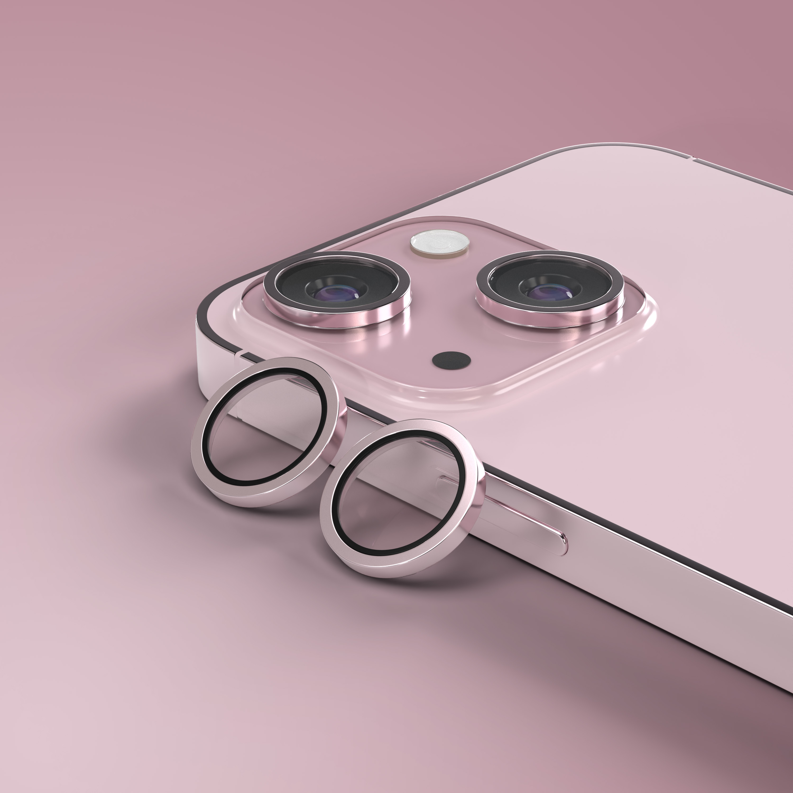 Due anelli protettivi rotondi e argentati giacciono davanti al retro di un telefono rosa.