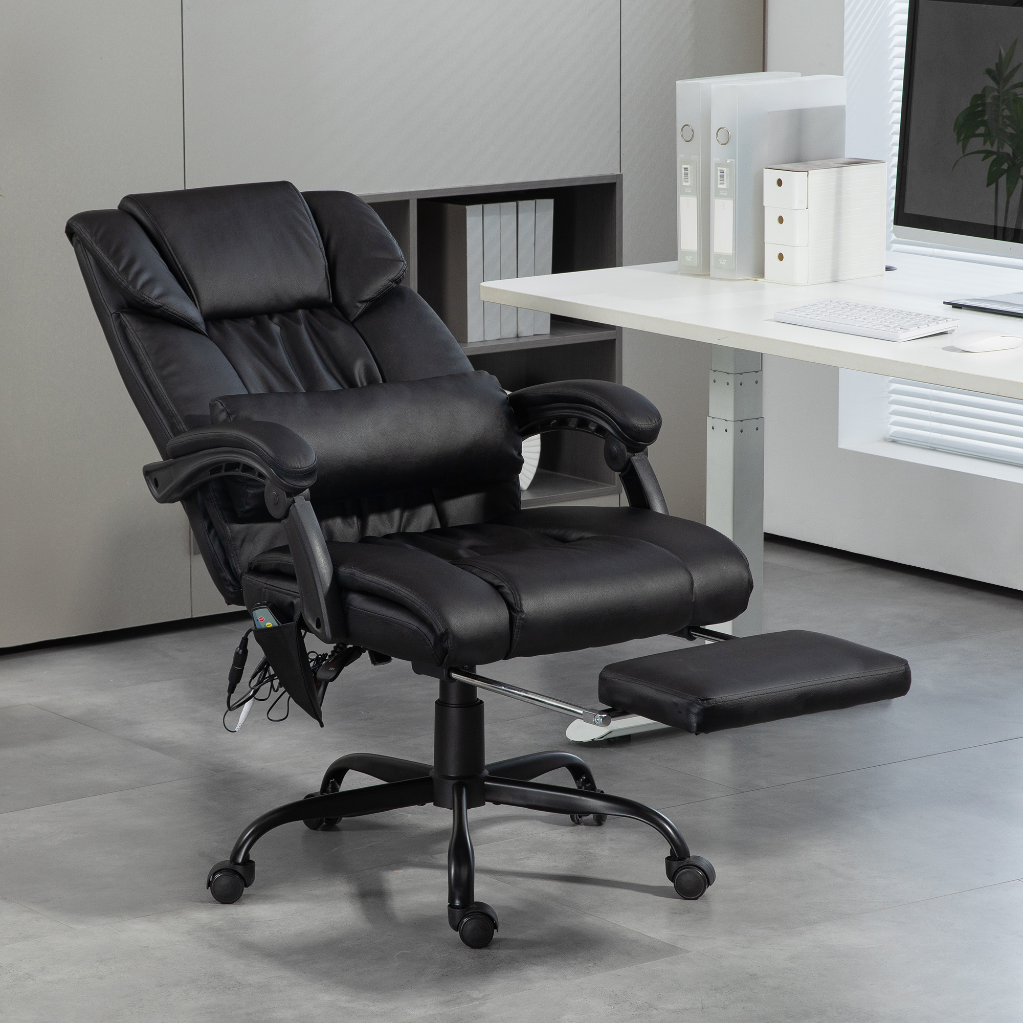 Silla ejecutiva negra con reposapiés y reposacabezas en suelo gris.
