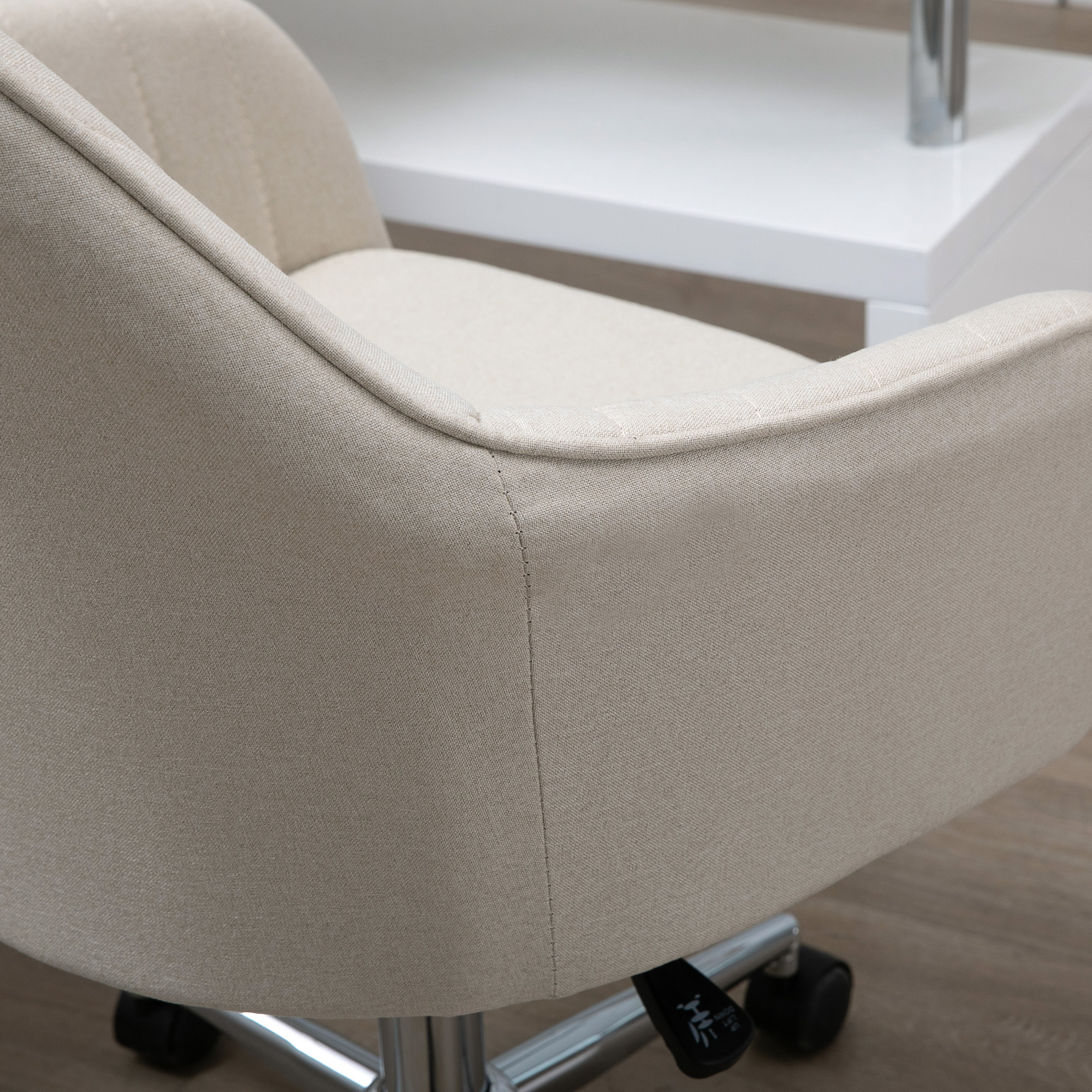 Silla de oficina beige de tela con ruedas metálicas sobre suelo de madera.