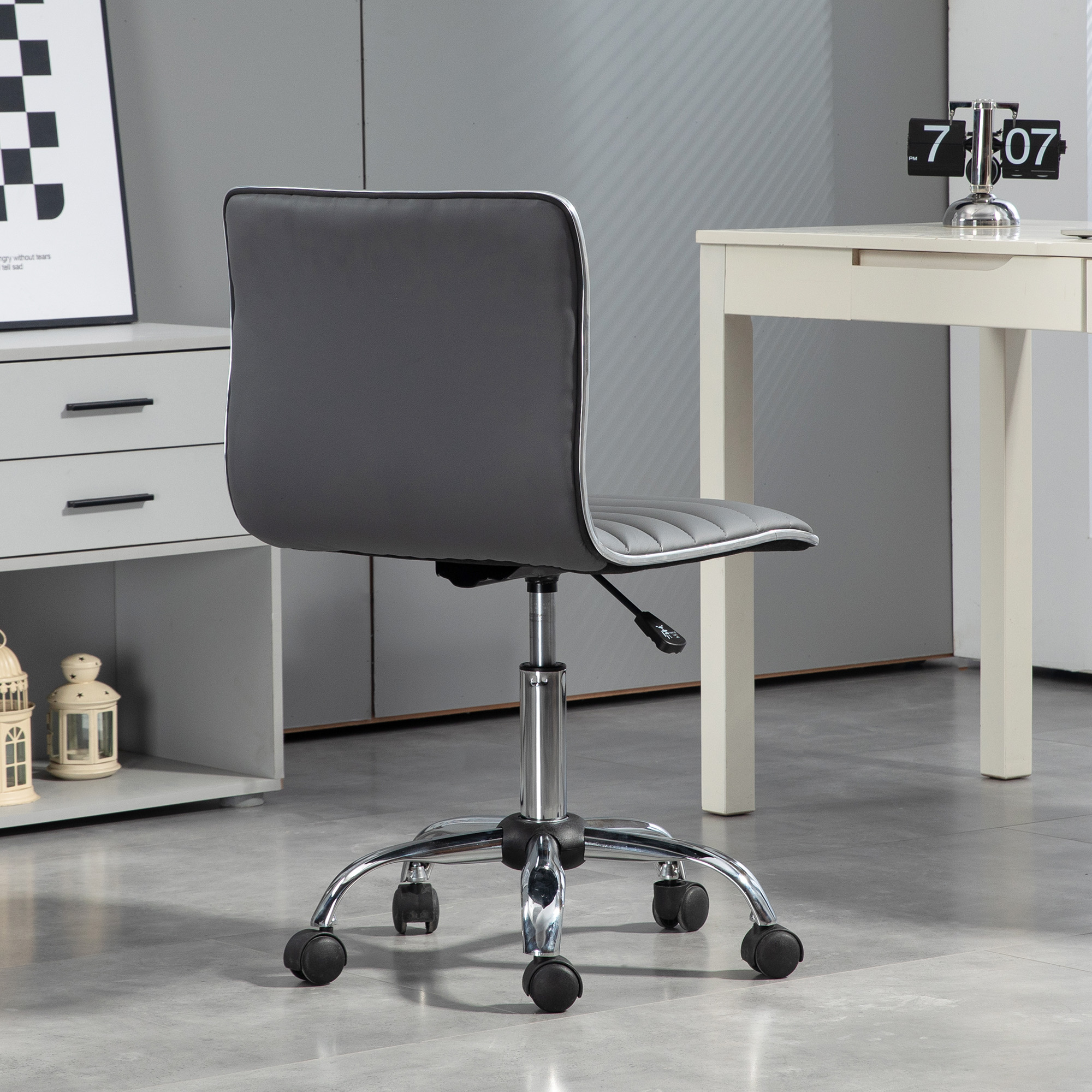 Una silla de oficina gris con base cromada y ruedas sobre suelo gris.