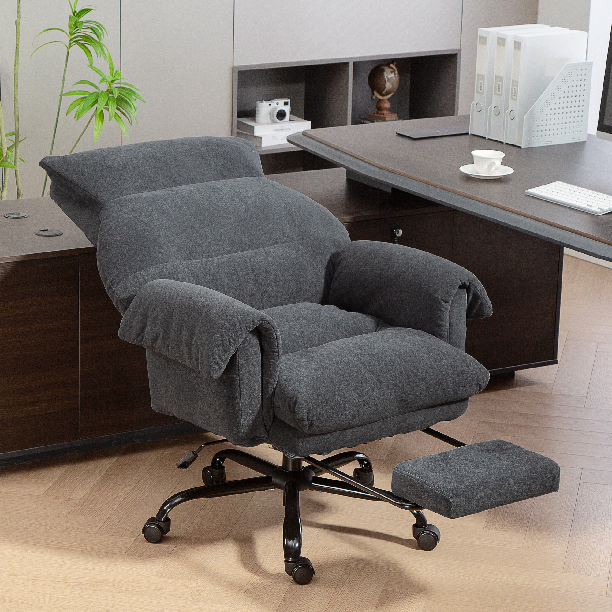 Una cómoda silla de oficina gris con reposapiés extensible está sobre un suelo de madera.