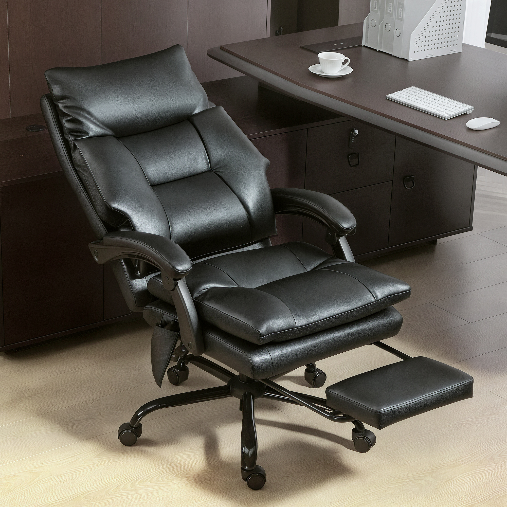 Silla de oficina de cuero negra con reposapiés frente a un escritorio oscuro.