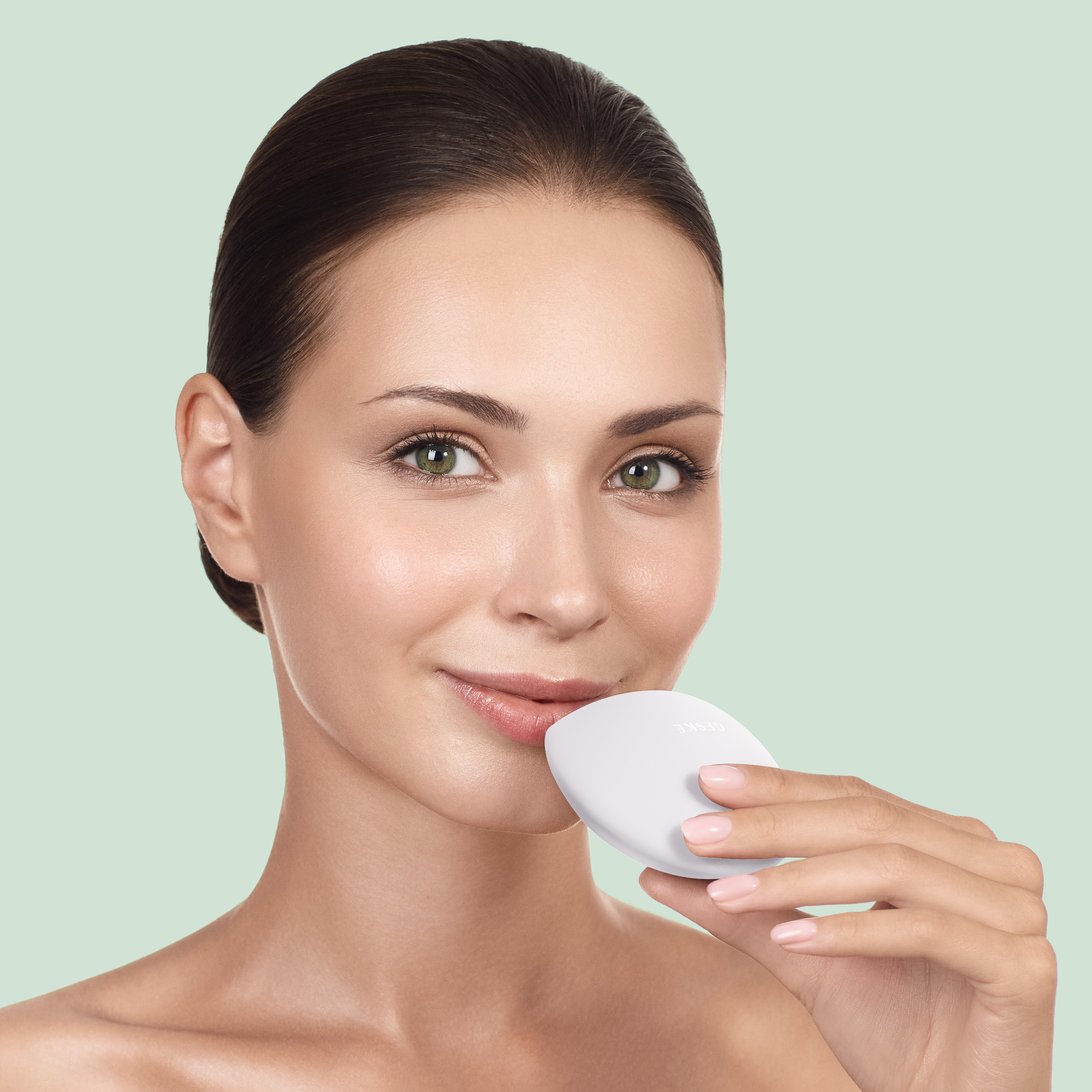 Donna con occhi verdi tiene un dispositivo bianco vicino alla bocca, sfondo verde pallido.