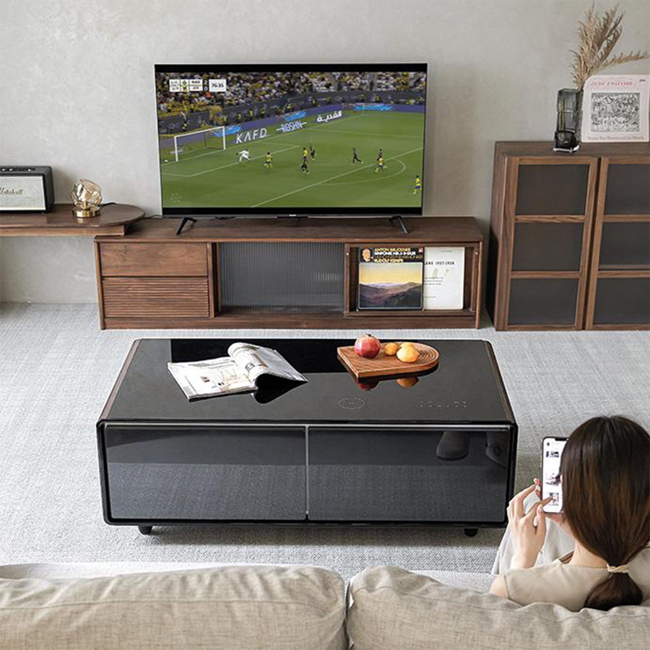 Futbol maçı gösteren TV'li ve telefonunu kullanan bir kadının olduğu oturma odası.