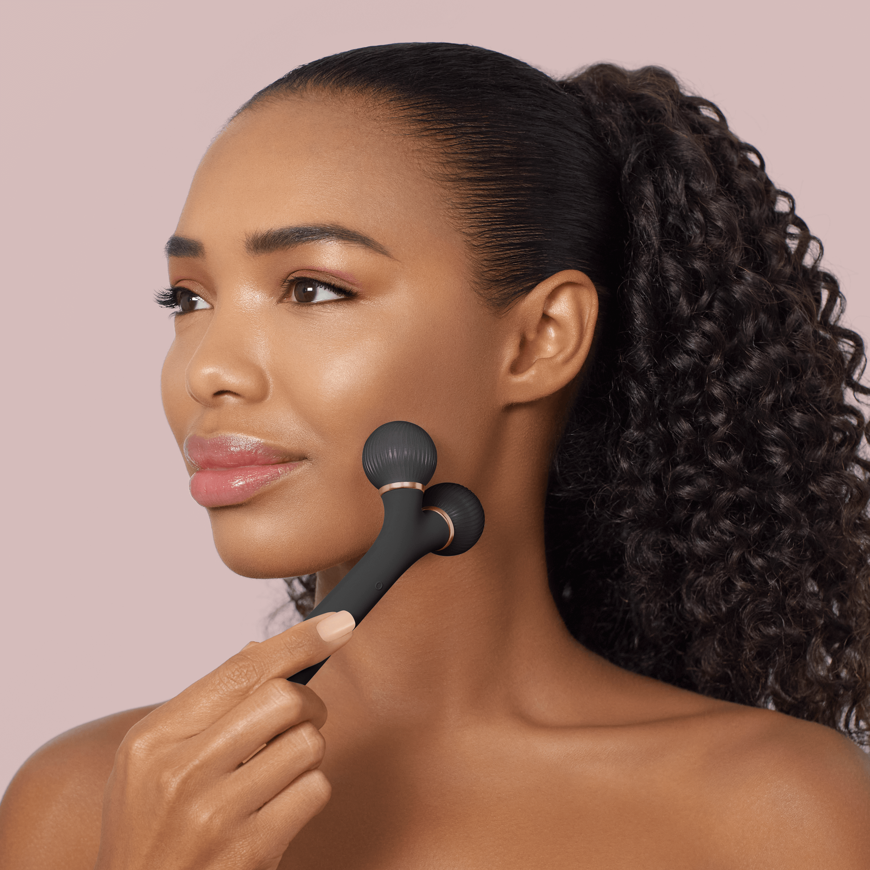 Una donna dai capelli scuri usa uno strumento massaggiante nero sul viso.