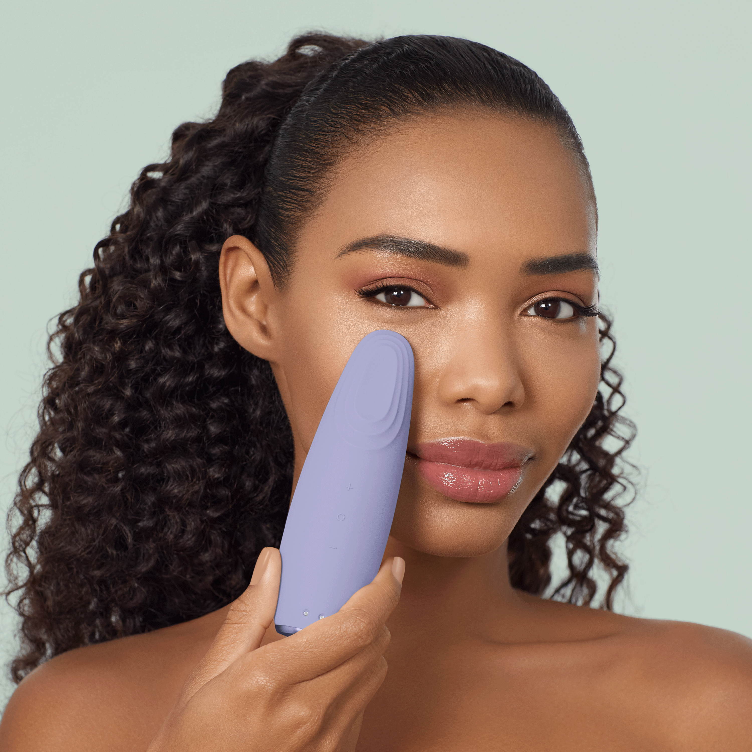 Una donna con capelli ricci scuri tiene un dispositivo di bellezza viola.