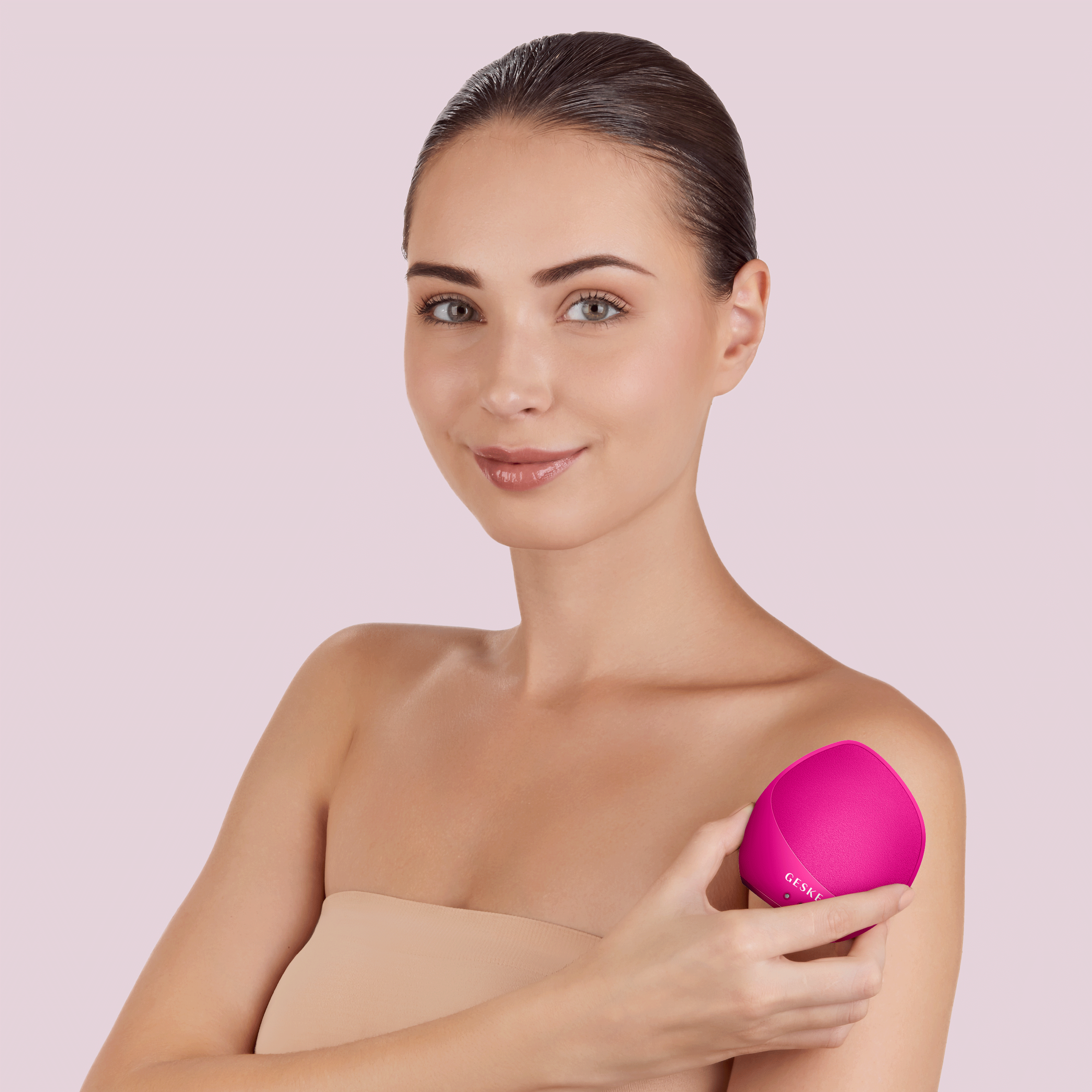 Bir kadın pembe bir cilt bakım cihazını omzuna tutuyor.