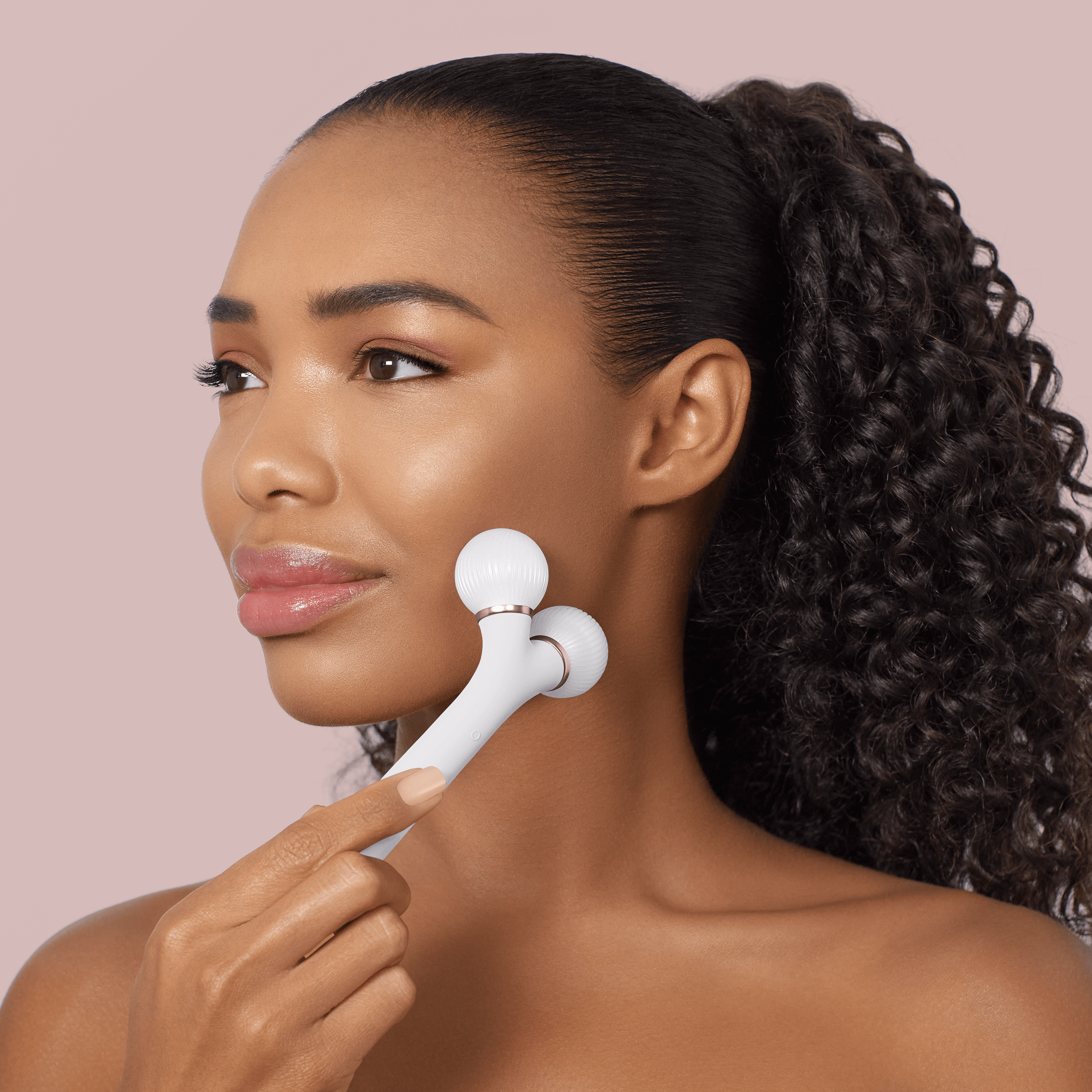 Una donna con capelli ricci scuri usa un rullo di bellezza bianco sulla guancia.