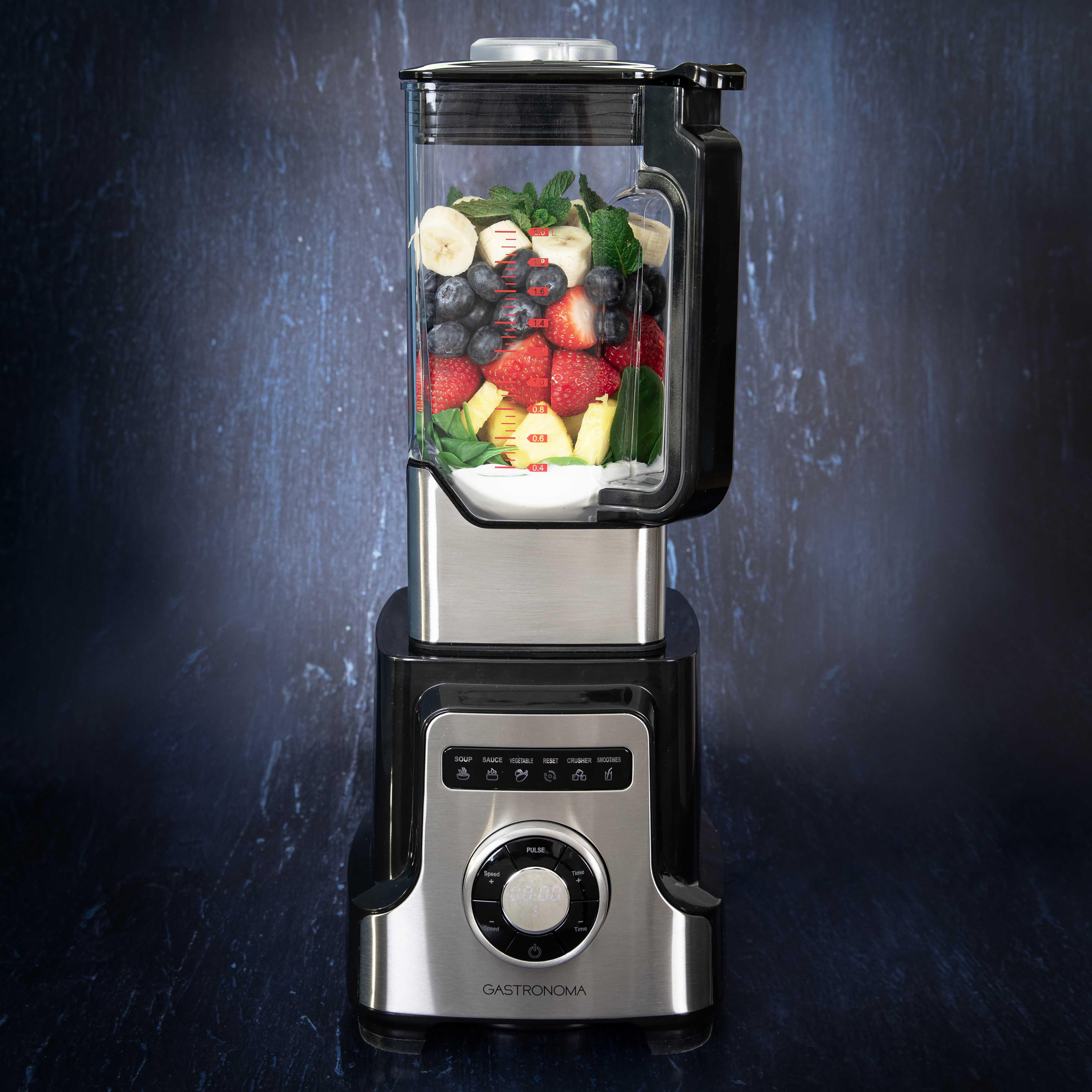 Czarno-srebrny blender Gastronoma wypełniony kolorowymi owocami, w tym truskawkami, jagodami, bananami i ananasem, na ciemnoniebieskim tle.