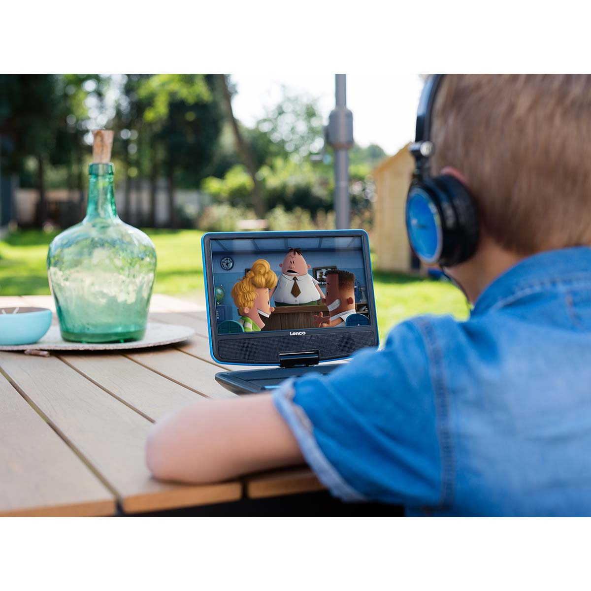 Chłopiec ogląda kreskówkę na przenośnym odtwarzaczu DVD na zewnątrz, nosząc niebieskie słuchawki.