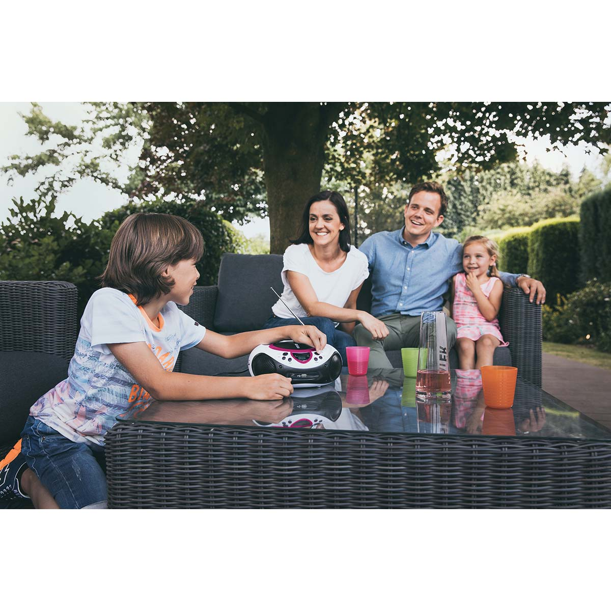 Une famille assise sur un canapé extérieur écoute de la musique sur une radio portable.