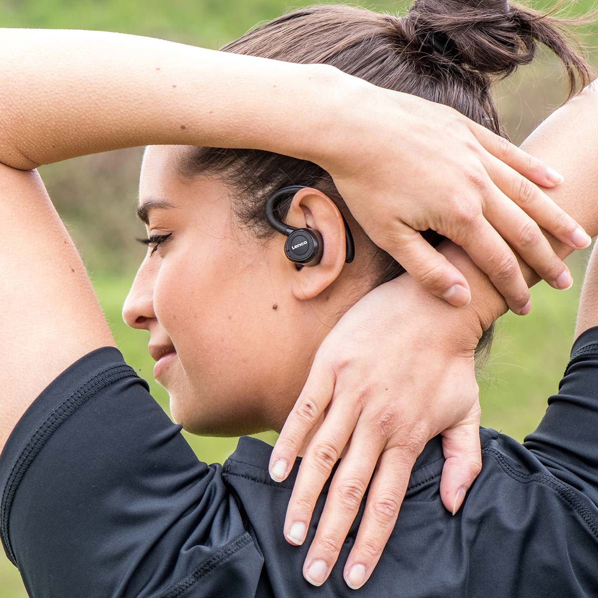 Mujer con auriculares se estira el cuello al aire libre.