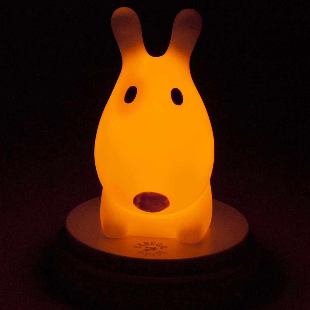 Una lámpara de noche naranja con forma de conejito brilla en la oscuridad.