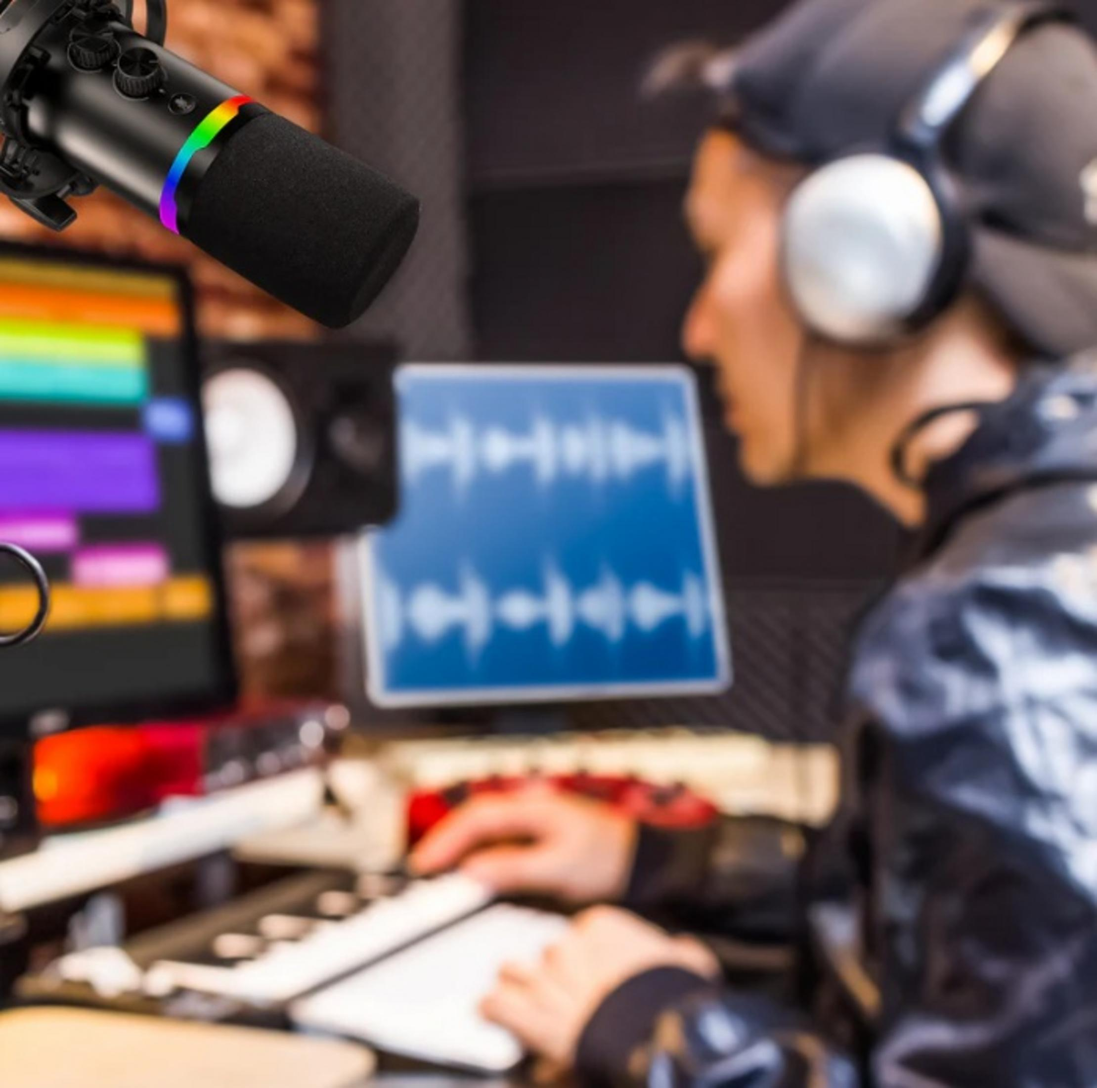 Un microfono con LED arcobaleno, un uomo con cuffie alla tastiera in uno studio.