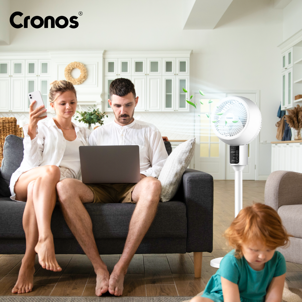 Para siedzi na kanapie z laptopem i telefonem. Dziecko bawi się na podłodze, w pobliżu stoi wentylator.