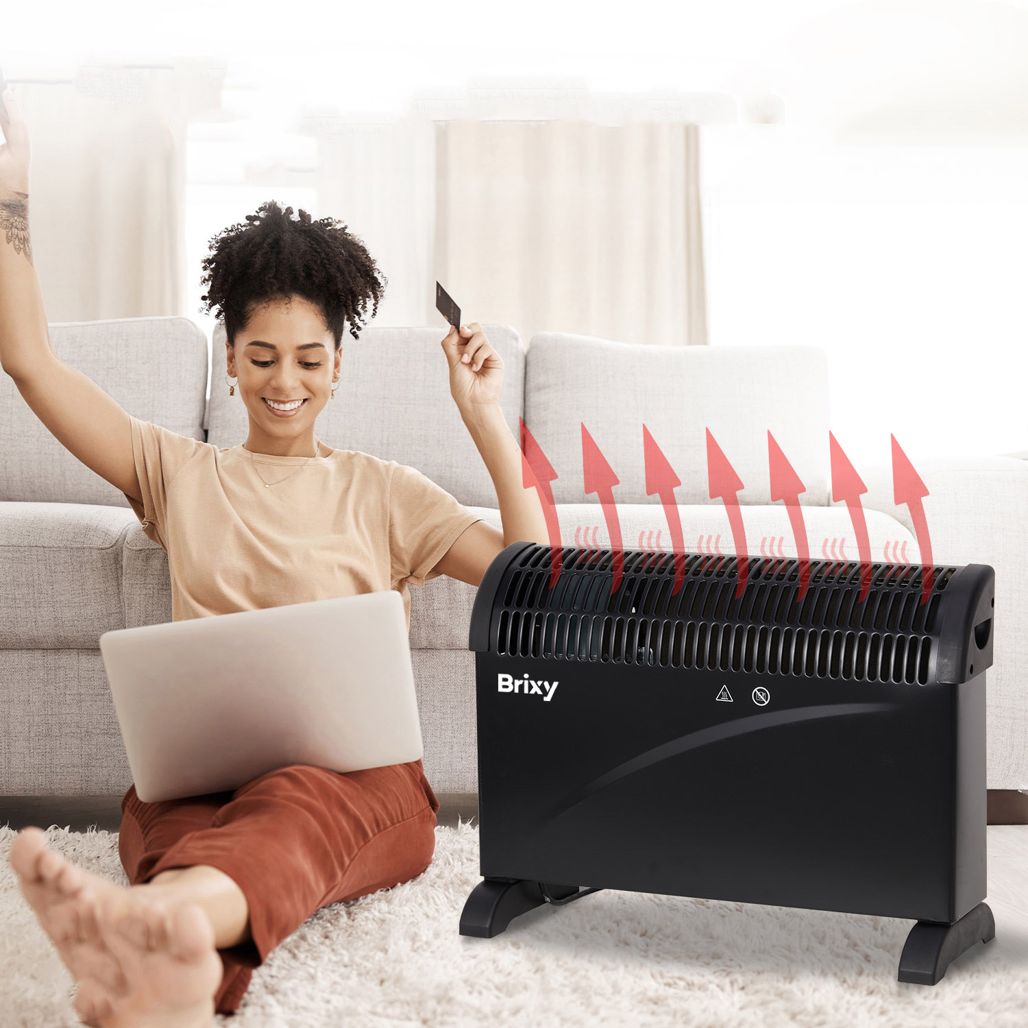 A woman sits on the floor using a laptop, next to a heater with red arrows.