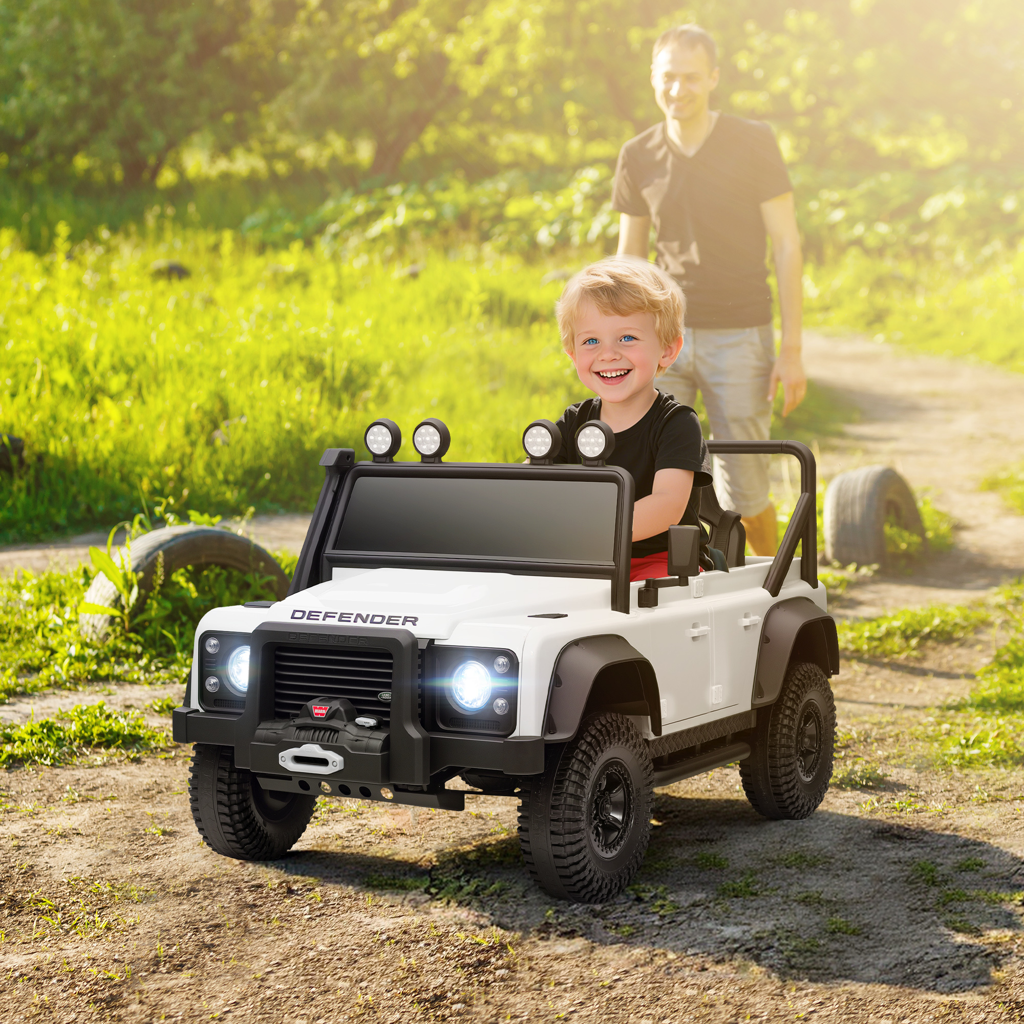 Un niño en un coche de juguete blanco con un hombre detrás al aire libre.