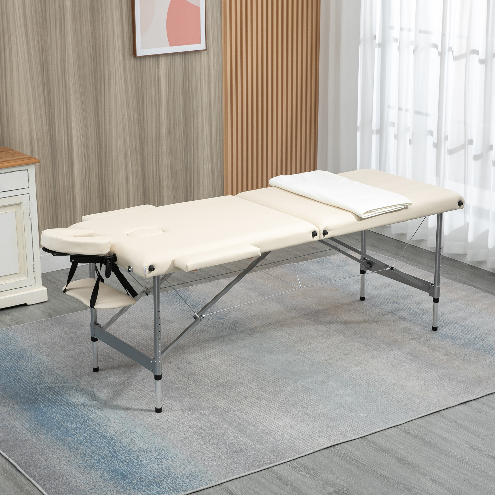 Una camilla de masaje portátil beige claro con reposacabezas ajustable y toalla blanca.