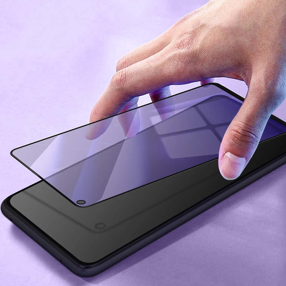 Mano applica pellicola protettiva su smartphone scuro su sfondo viola.