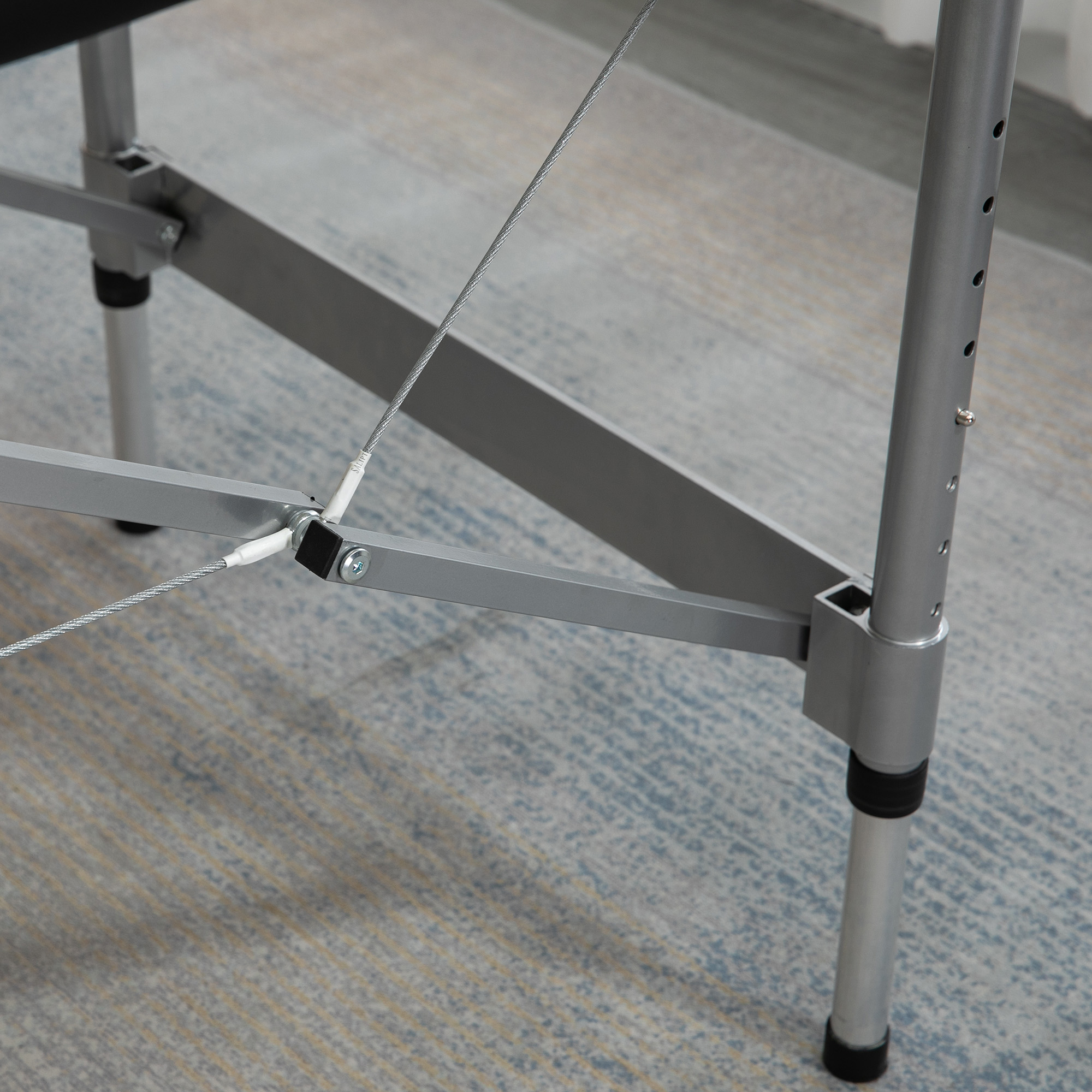 Marco metálico gris con cables y pata ajustable sobre alfombra.