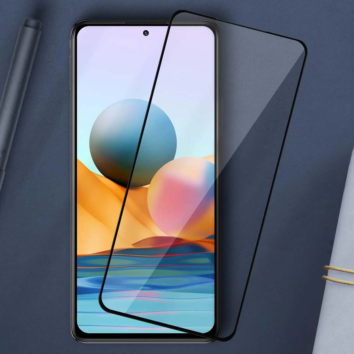 Uno smartphone con proteggi schermo e una penna accanto su sfondo blu.
