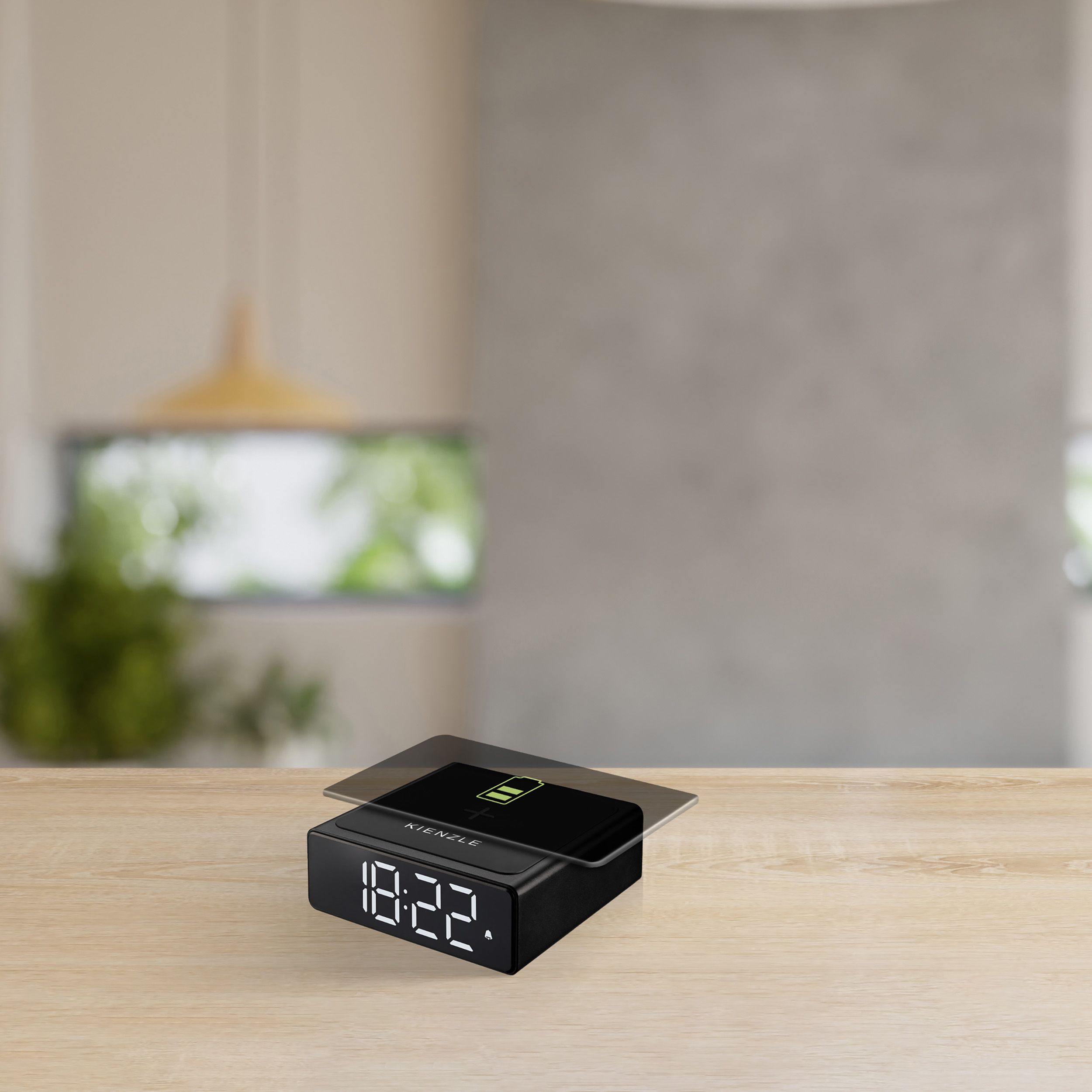 Reloj despertador digital negro con icono de batería cargando en mesita.