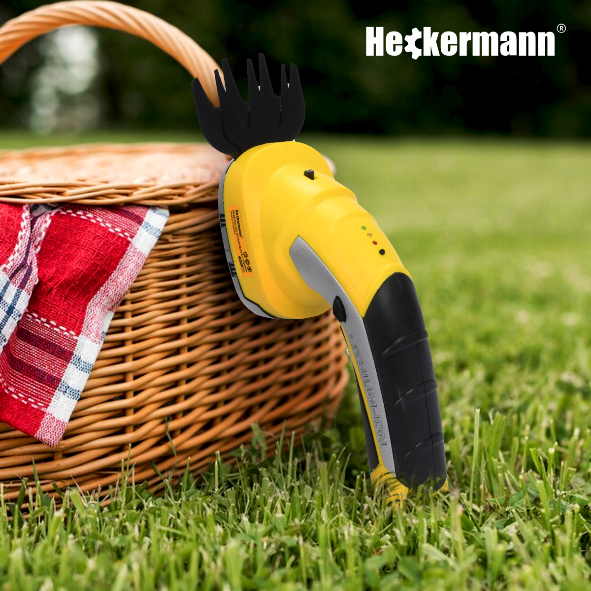Żółty trymer ręczny obok koszyka piknikowego na trawie. Marka Heckermann.