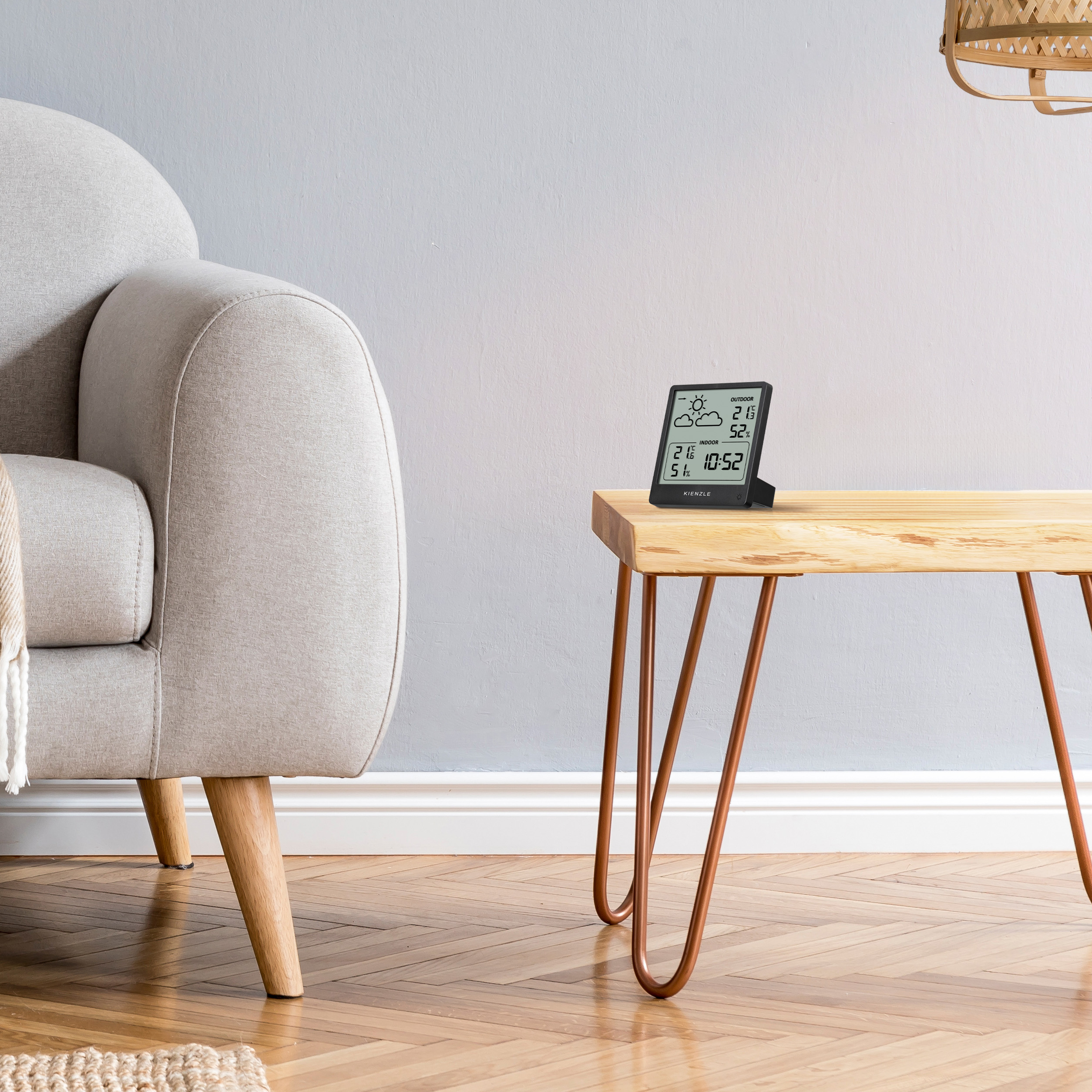 Una estación meteorológica digital sobre una mesa de madera junto a un sillón.
