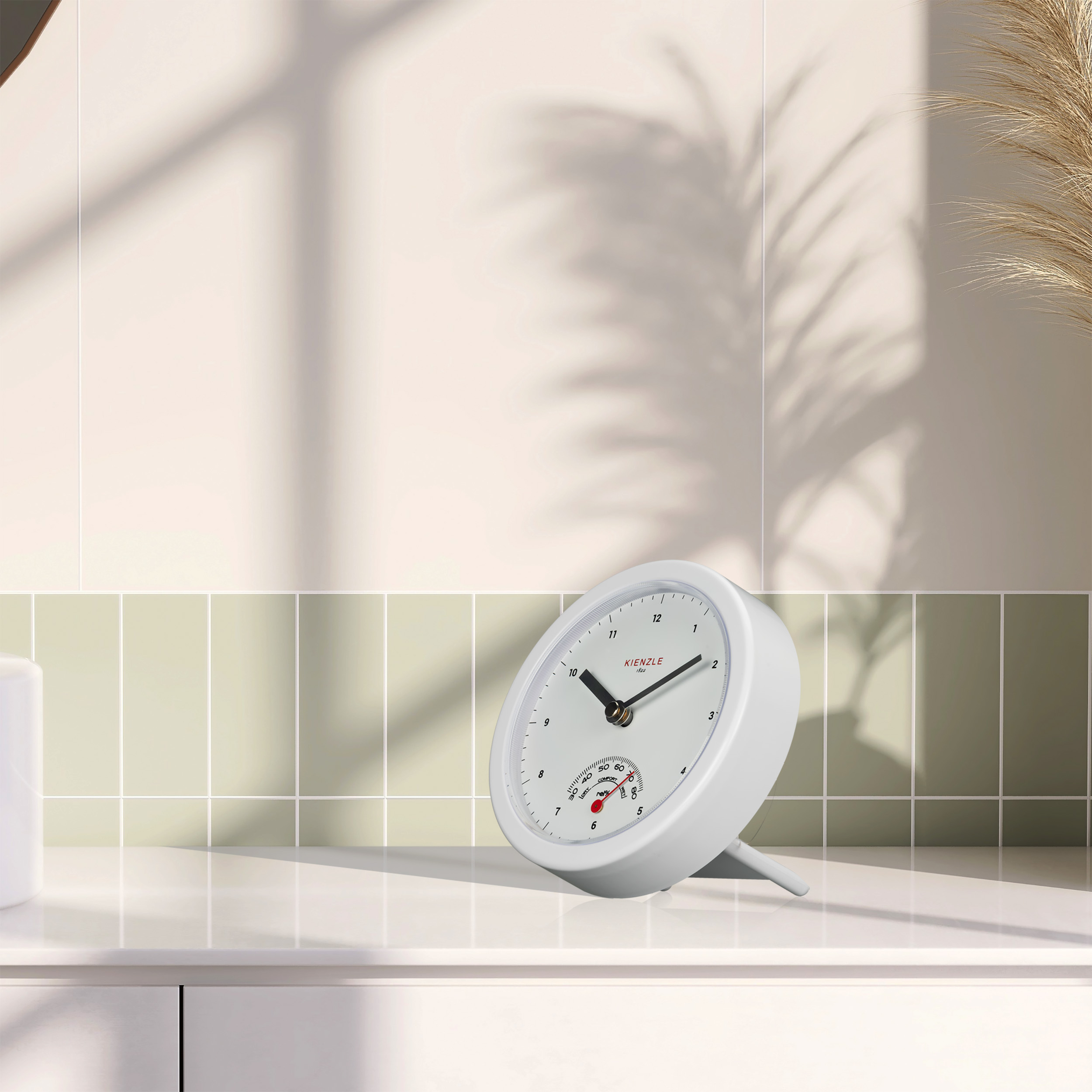 Un reloj Kienzle blanco con termómetro descansa sobre una superficie blanca.