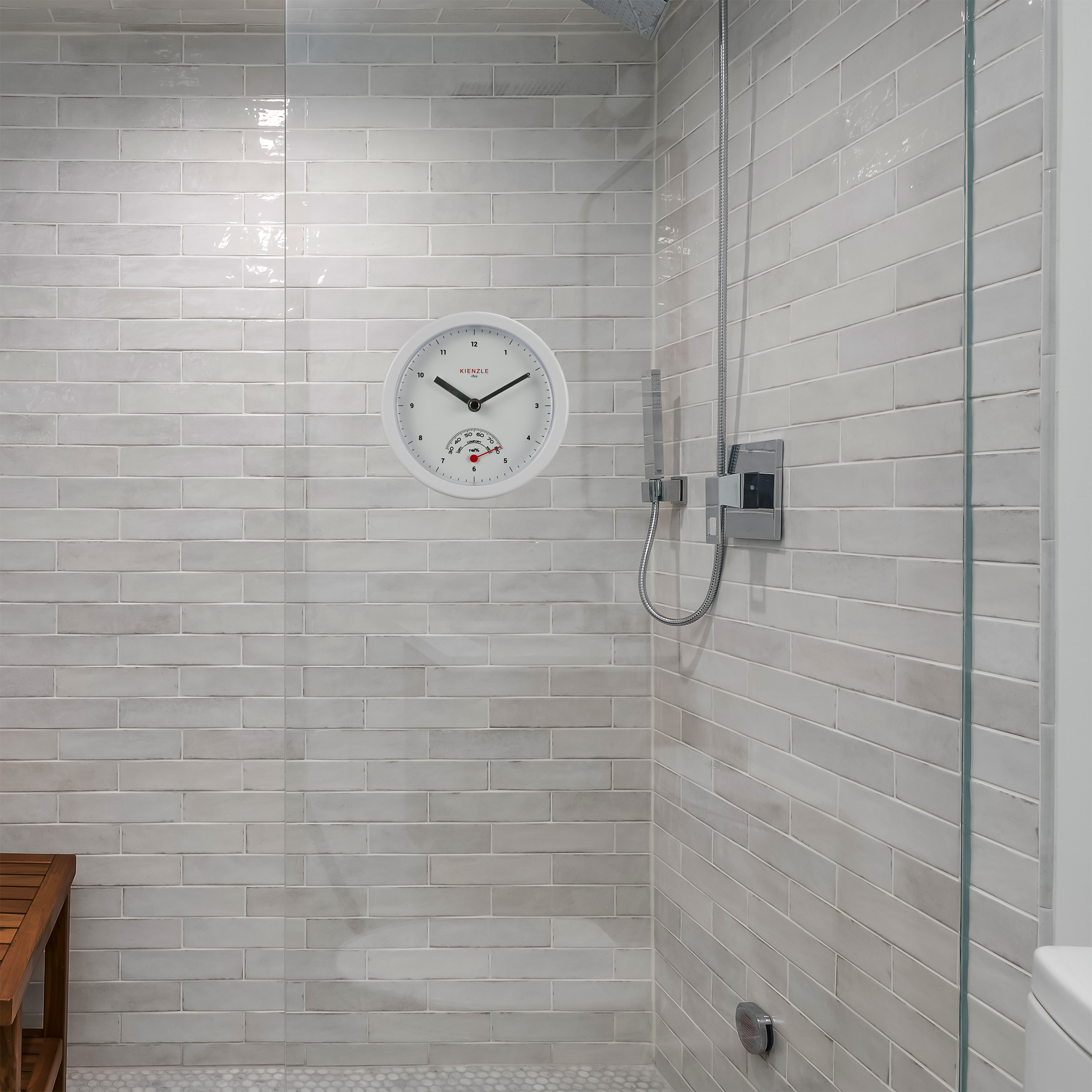 Pared de ducha con azulejos blancos, alcachofa, reloj y termómetro.