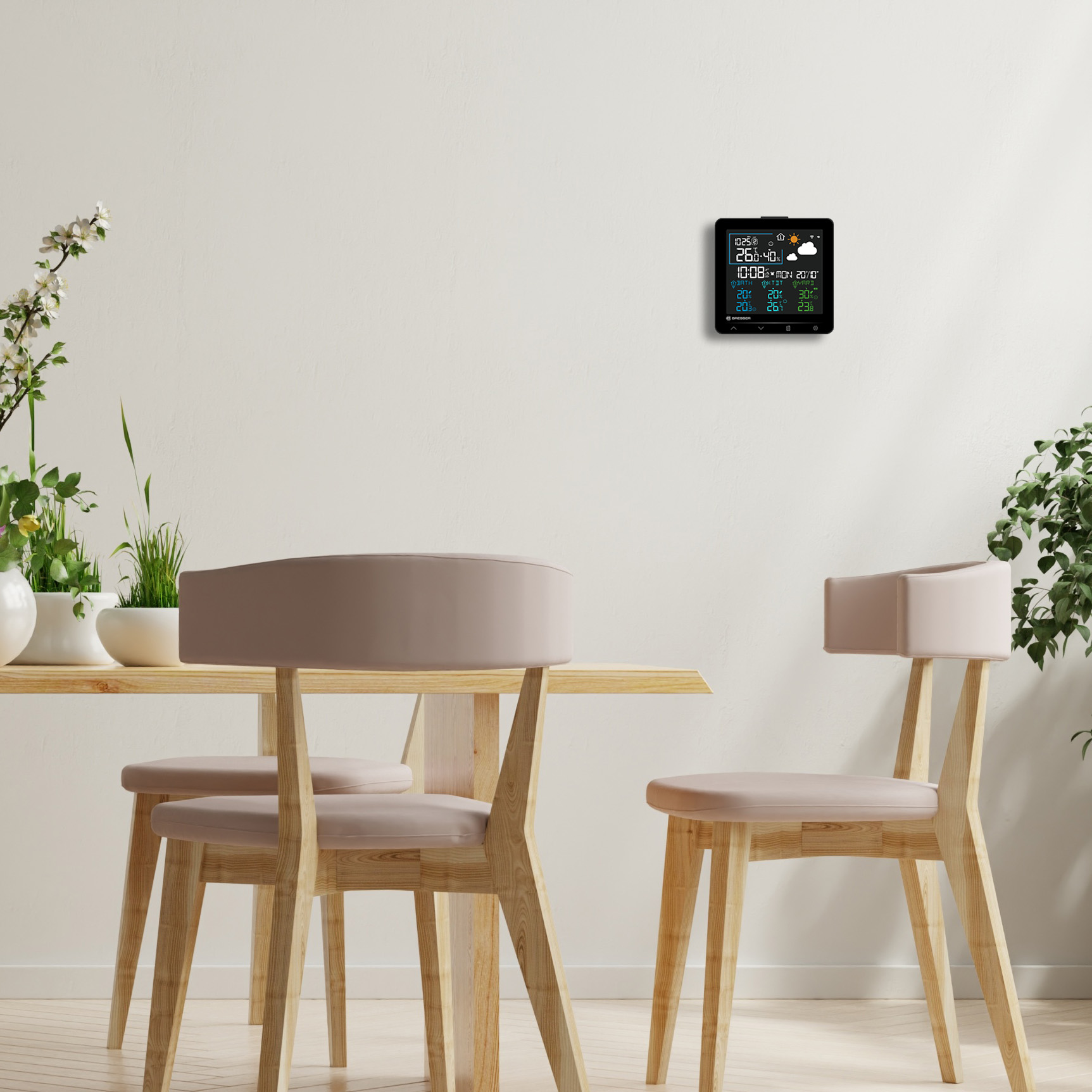 Estación meteorológica digital en pared blanca sobre mesa de madera con sillas.