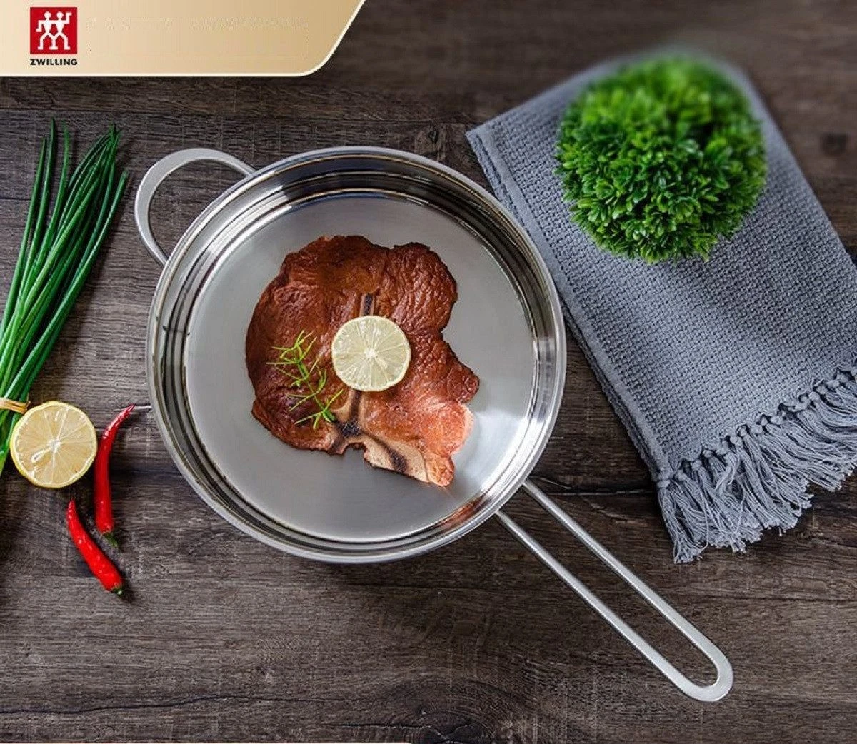 Ein gebratenes Steak mit Zitrone in einer Pfanne, daneben Frühlingszwiebeln, Chilis und ein Handtuch.