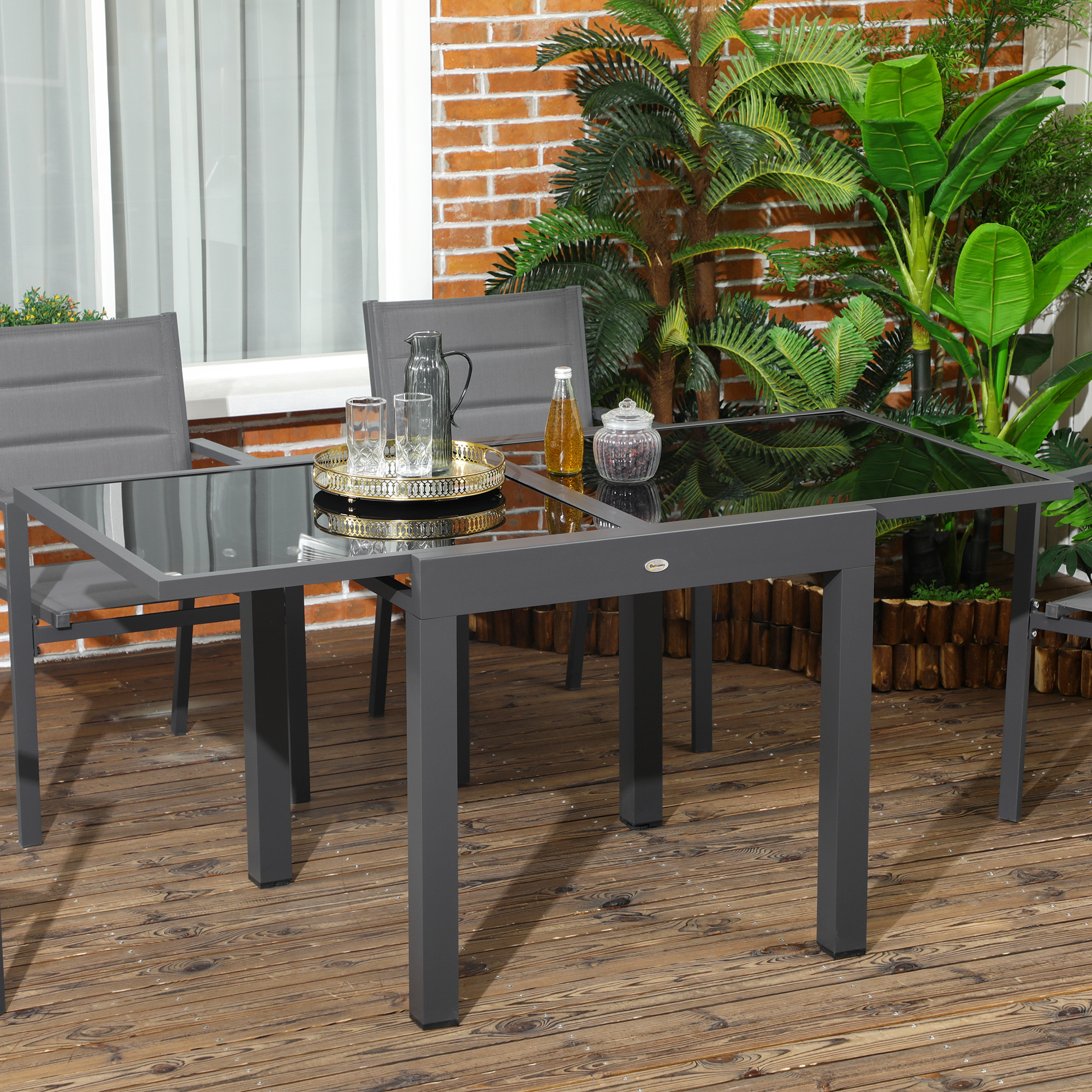 Una mesa gris de exterior con tapa de cristal y sillas sobre una terraza de madera.