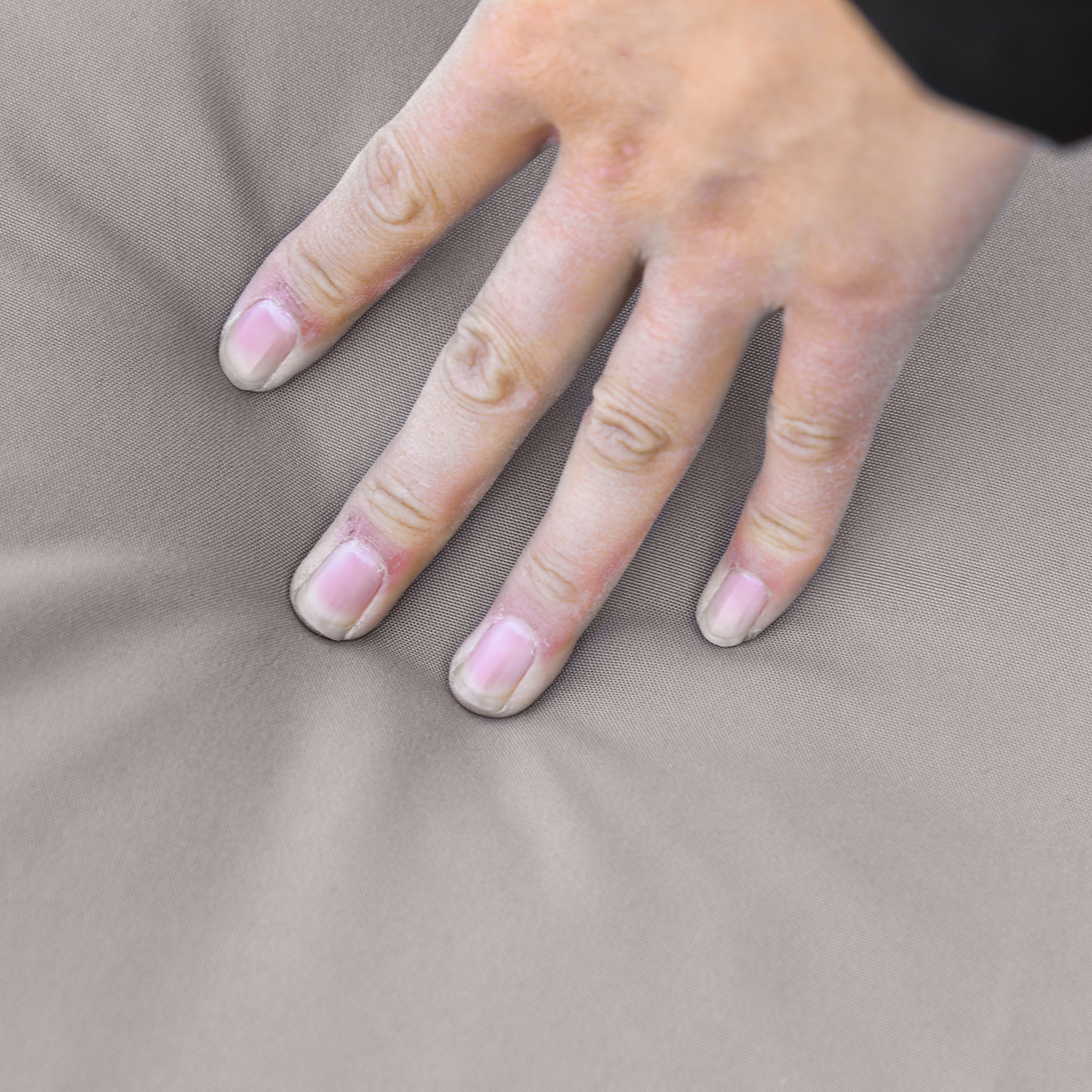 Una mano con unghie chiare preme su un tessuto grigio.