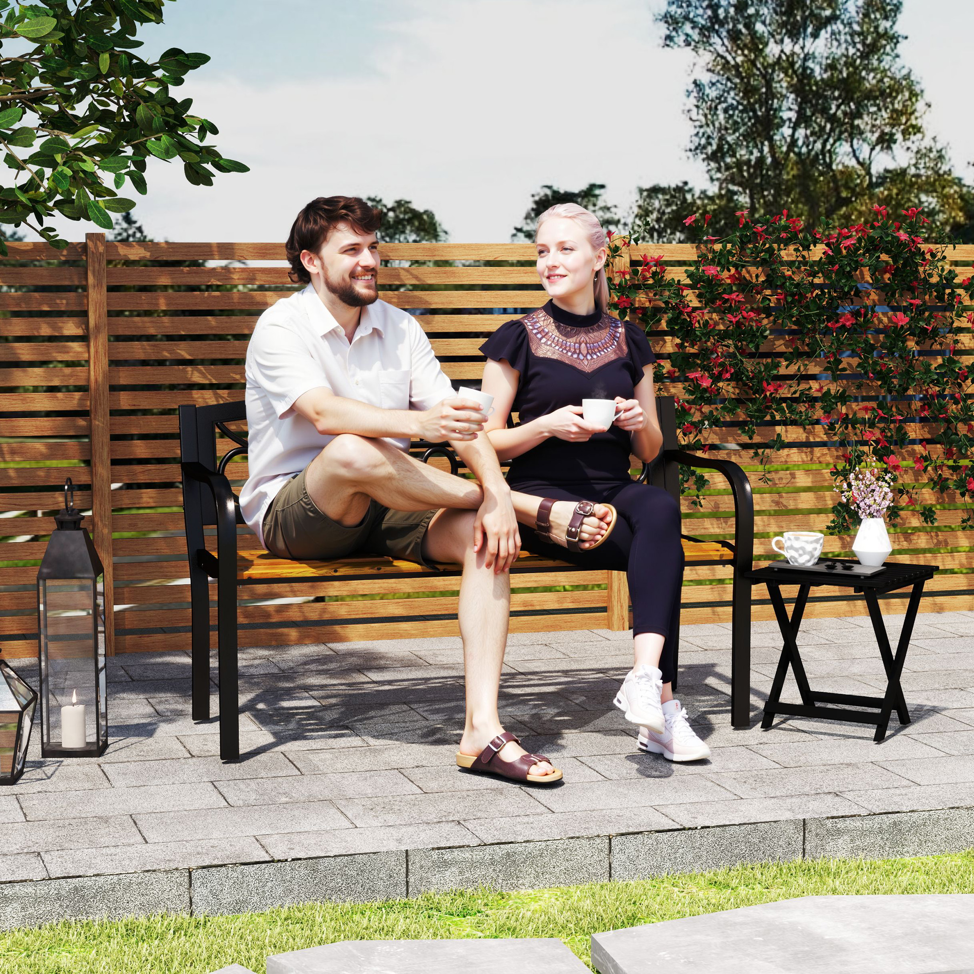 Una pareja sentada en un banco al aire libre bebiendo café. Valla de madera al fondo.
