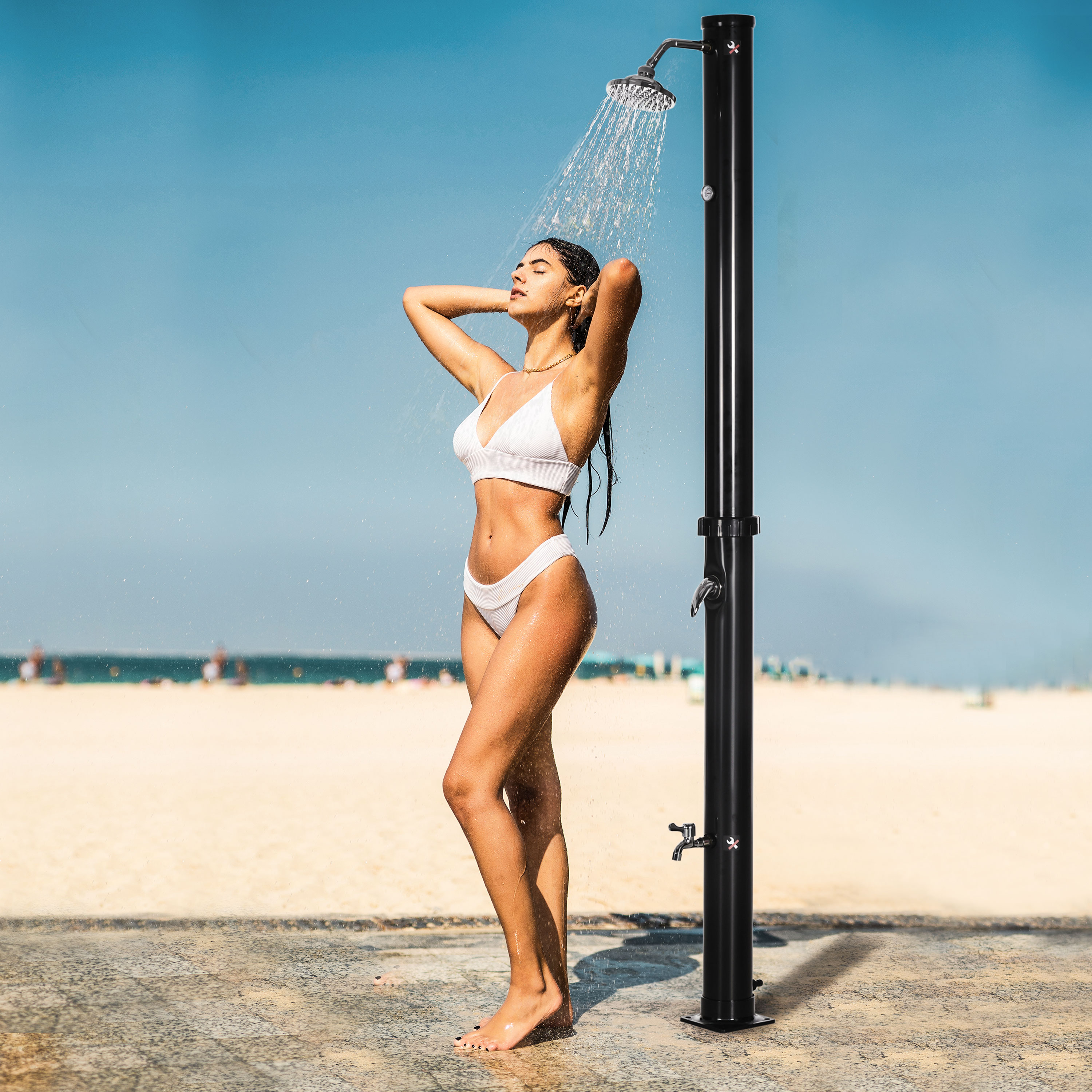 Mujer en bikini blanco duchándose en la playa.