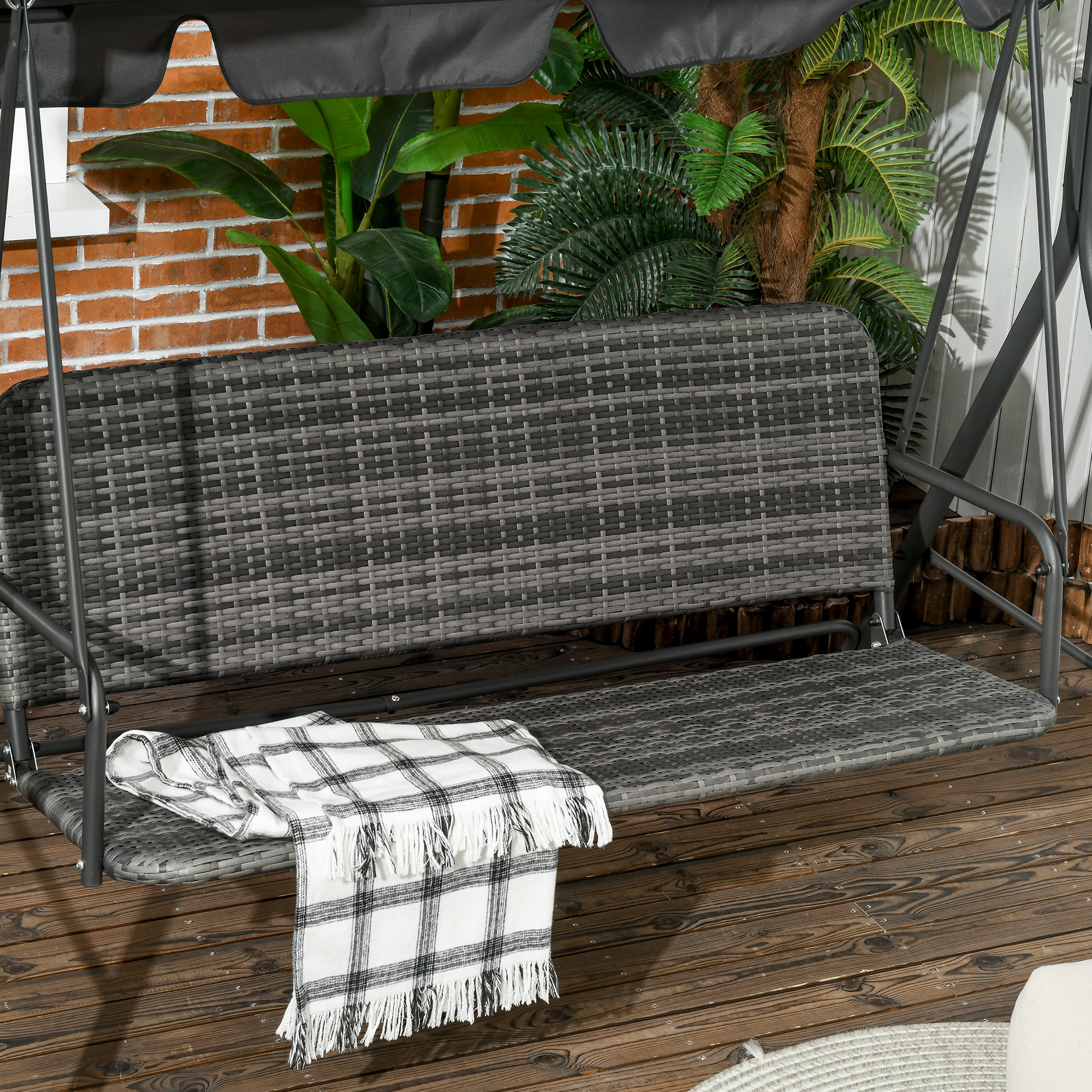 Altalena in rattan grigio con coperta a quadri su terrazza in legno, dietro piante.