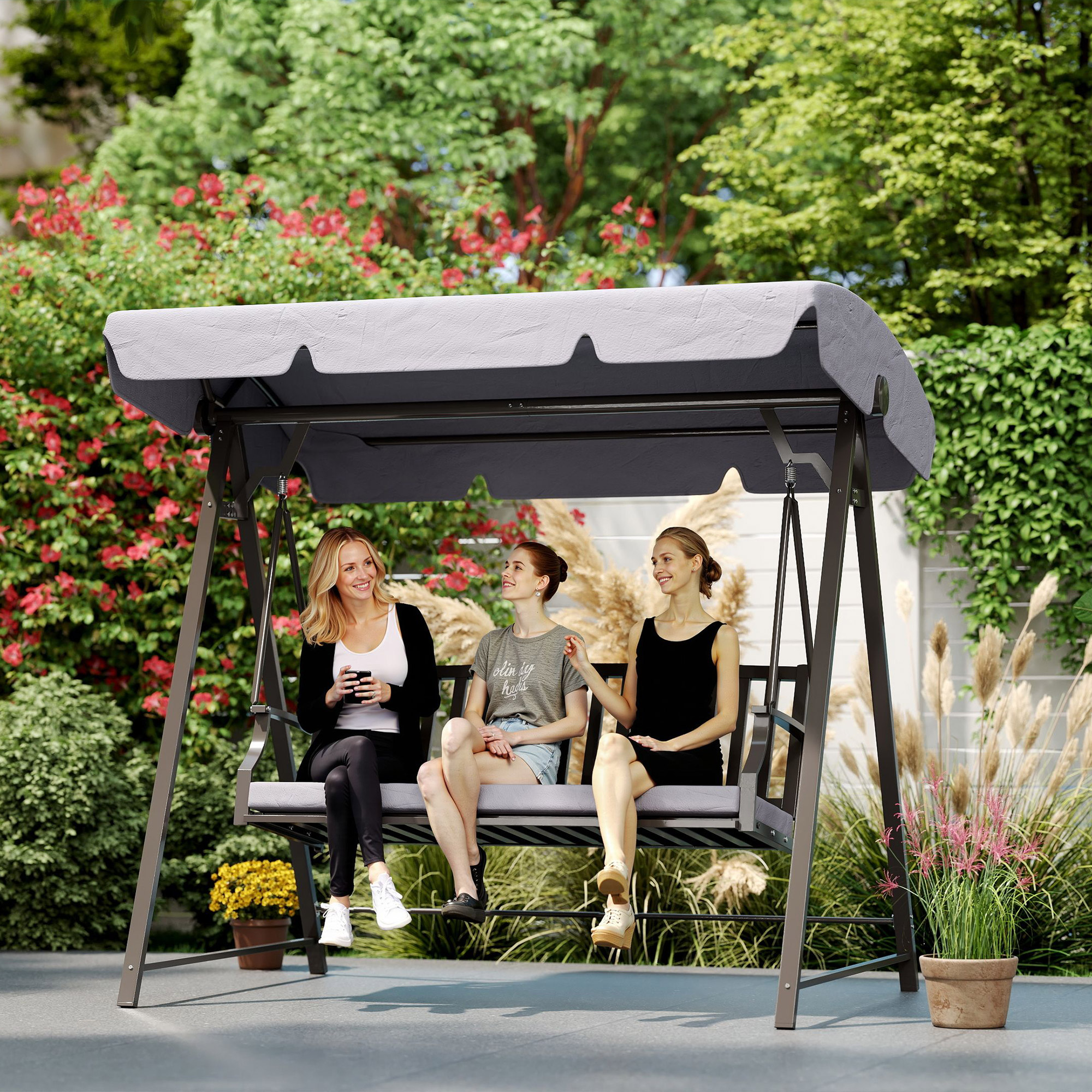 Tres mujeres sentadas en un columpio de jardín. Flores rojas florecen al fondo.