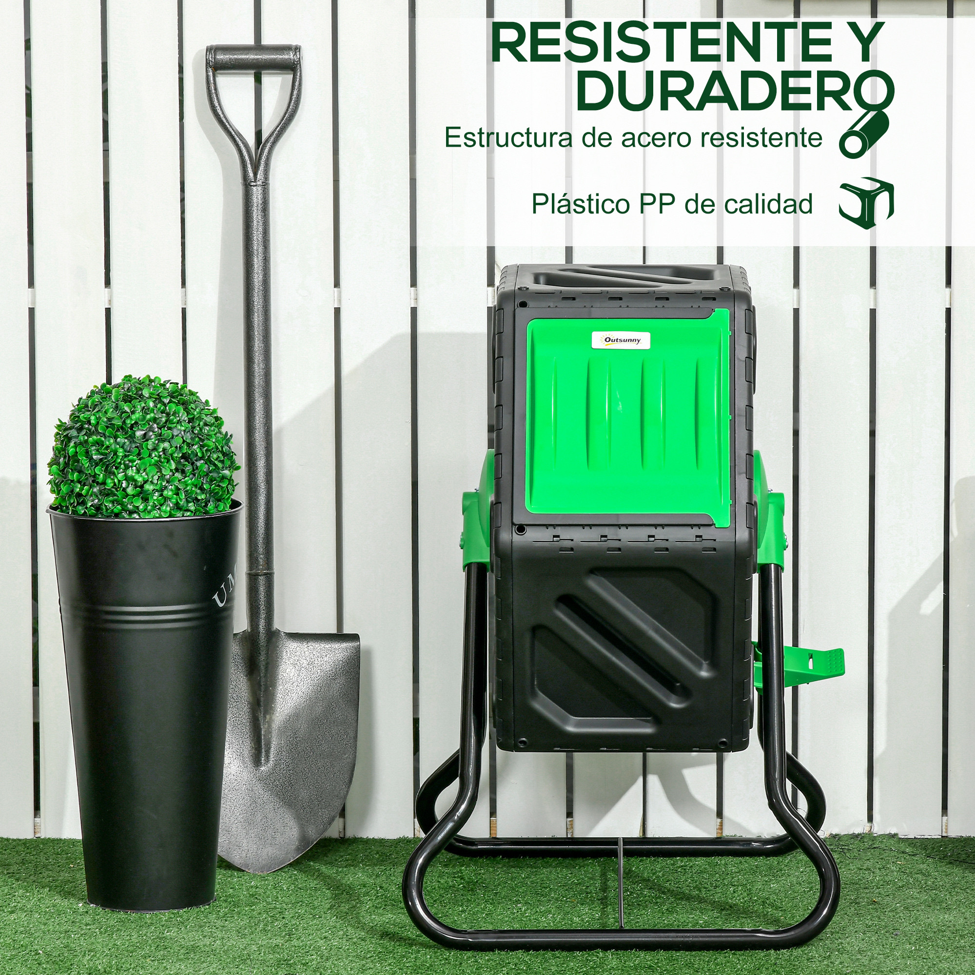 Un compostador, pala y planta artificial en maceta sobre césped artificial.