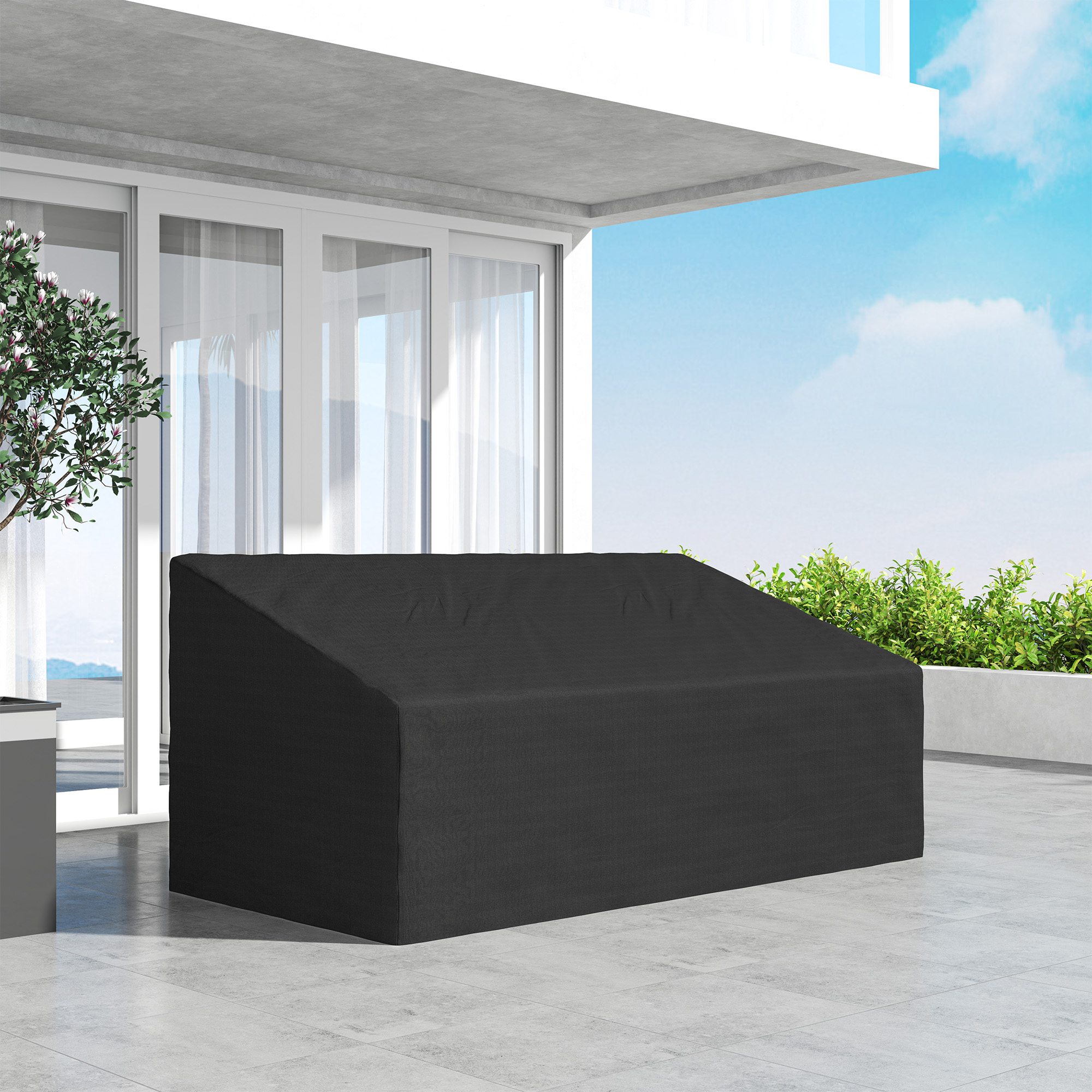 Una funda negra para muebles está en un patio embaldosado junto a una planta.