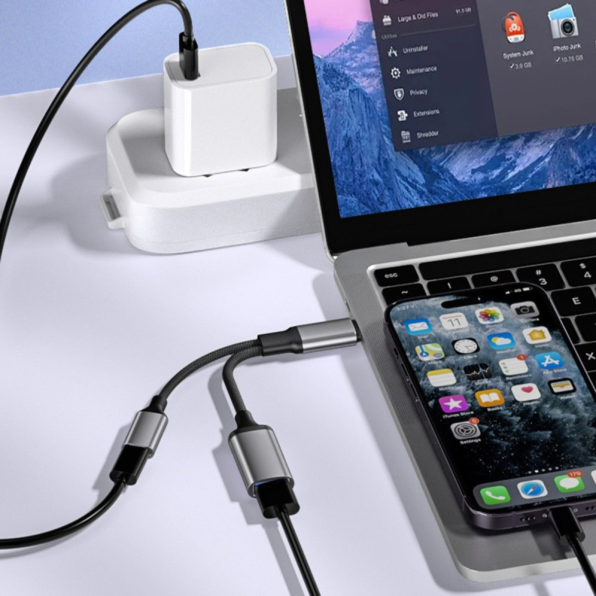 Ein Laptop, ein Telefon und ein Ladegerät sind über Kabel auf weißer Oberfläche verbunden.