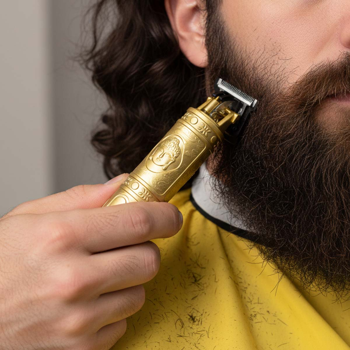 Recortadora de barba dorada con grabado de Buda sostenida por una mano recortando una barba.