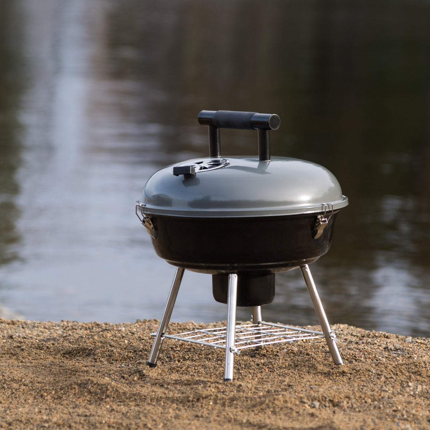 Een grijze grill staat op zand aan de waterkant.