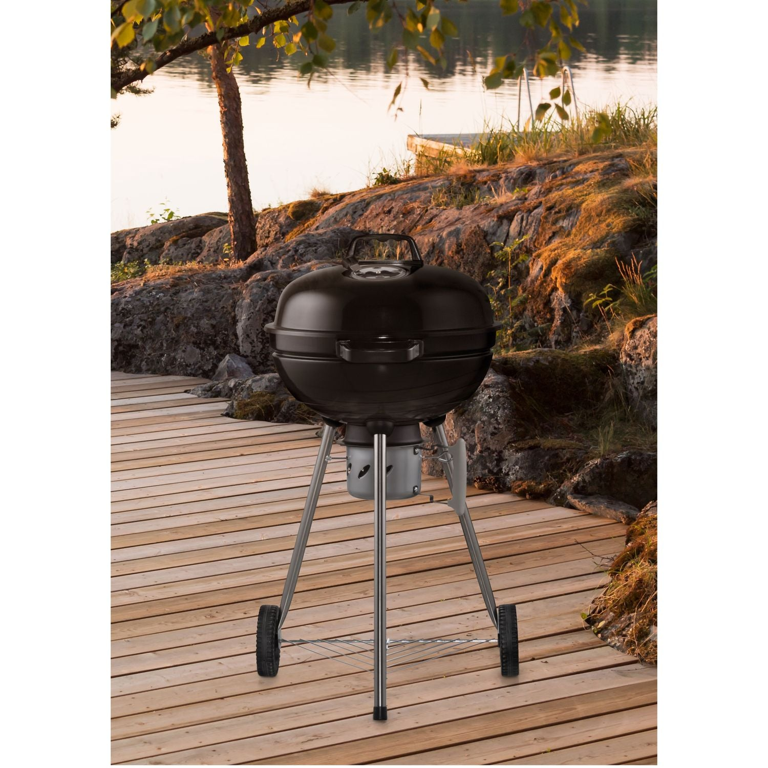 A black grill sits on a wooden deck by a lake.