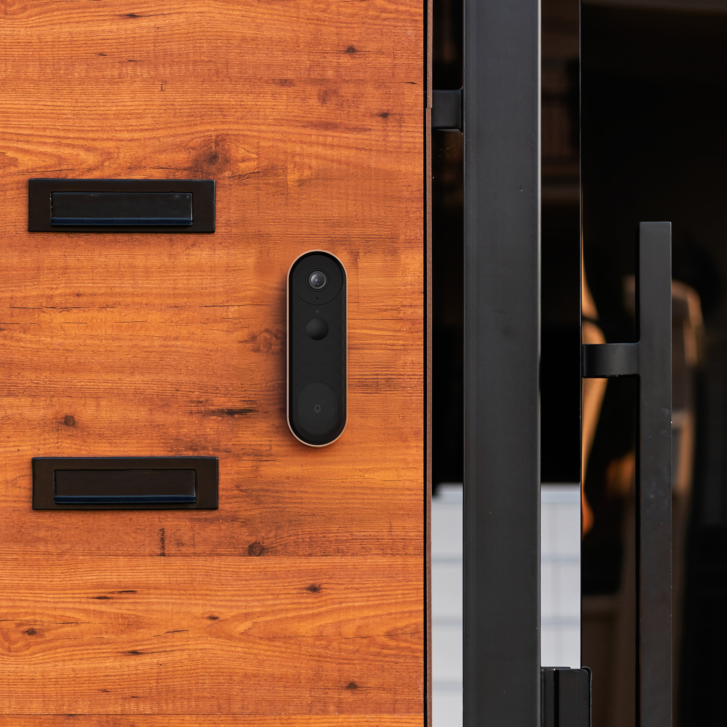 Porta d'ingresso in legno con campanello nero, telecamera e due fessure per lettere.