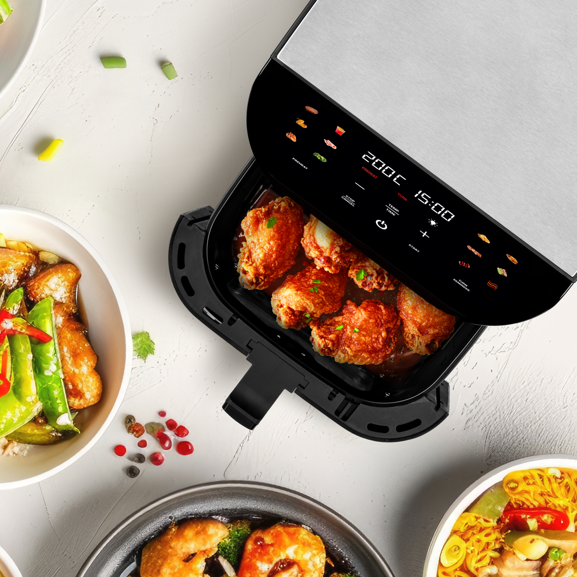 Una friggitrice ad aria con alette di pollo e ciotole di cibo accanto.