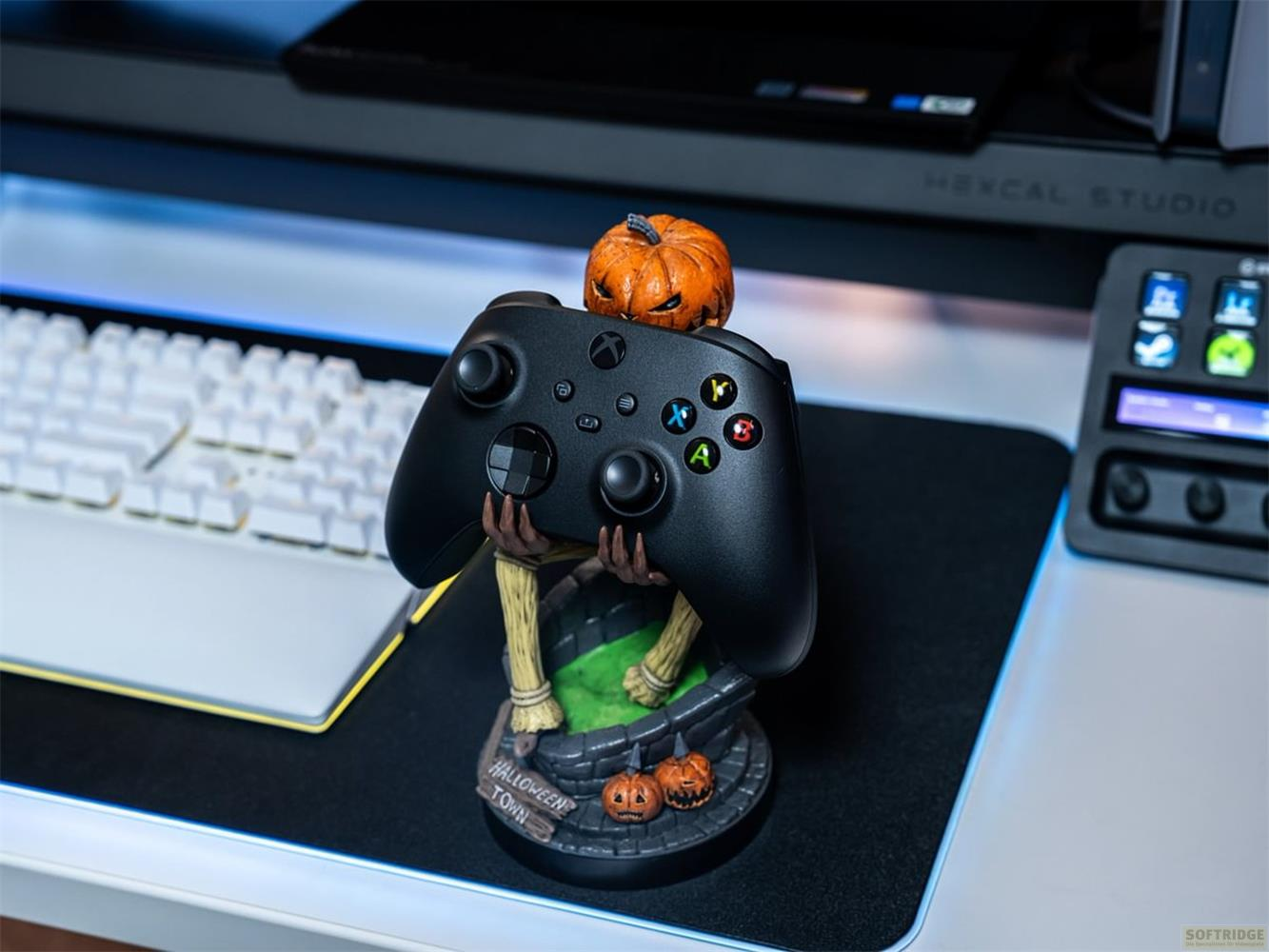 Un mando negro de Xbox se asienta sobre un soporte temático de Halloween con calabazas y una espeluznante escena de cementerio.