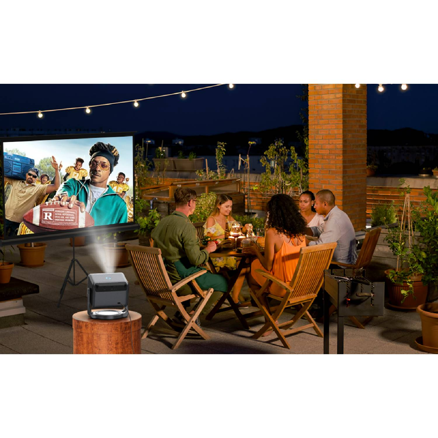 Ludzie jedzą kolację na zewnątrz, gdy projektor wyświetla film na ekranie.