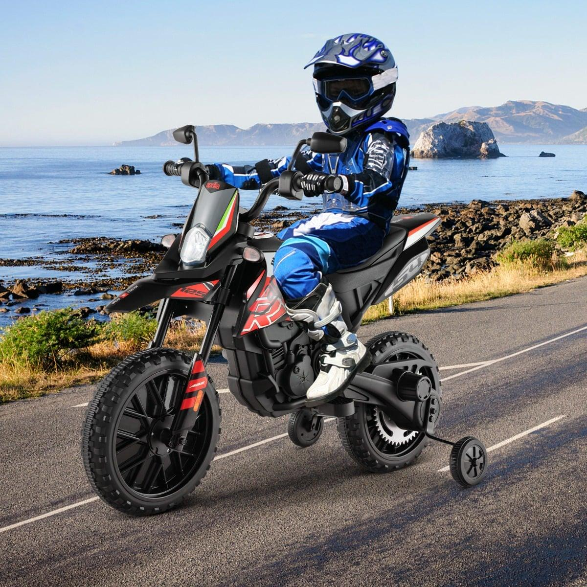 Niño con equipo de montar azul en una moto de cross negra con ruedas de entrenamiento en carretera costera.
