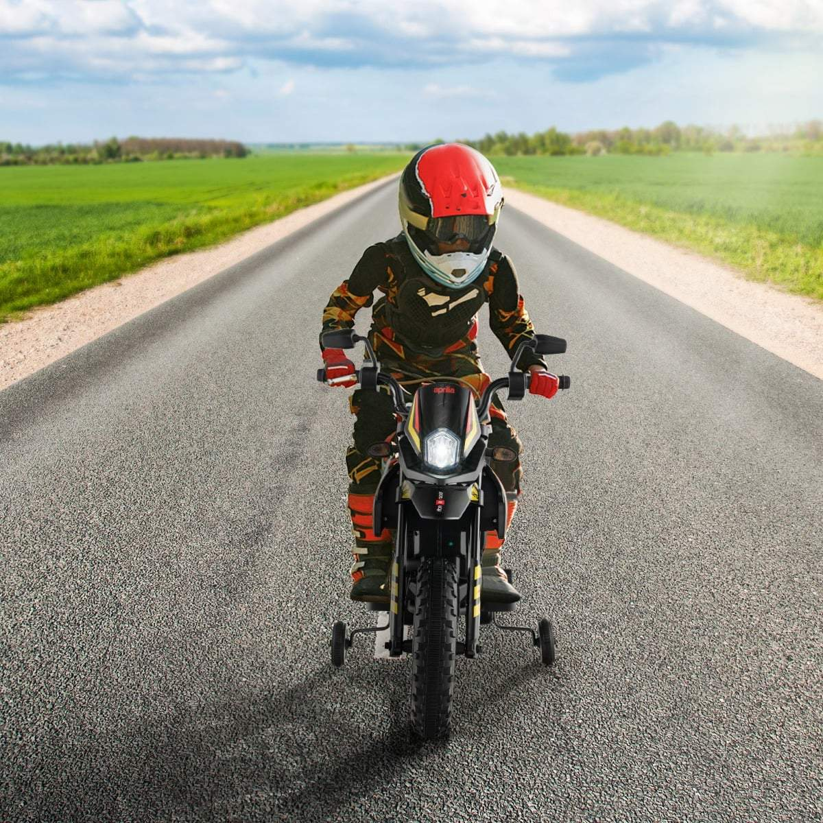 Un niño con equipo de protección monta una motocicleta con ruedas de entrenamiento en una carretera.